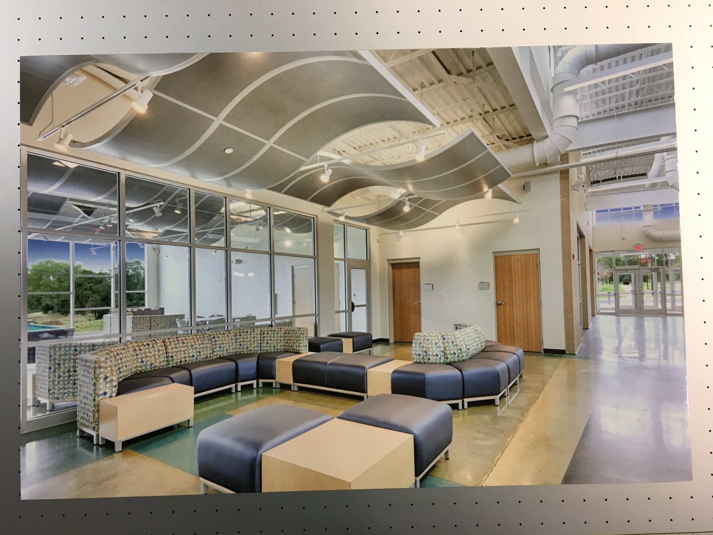 Modern lounge area with modular seating, patterned cushions, wood and leather furniture, large windows, and architectural ceiling design.