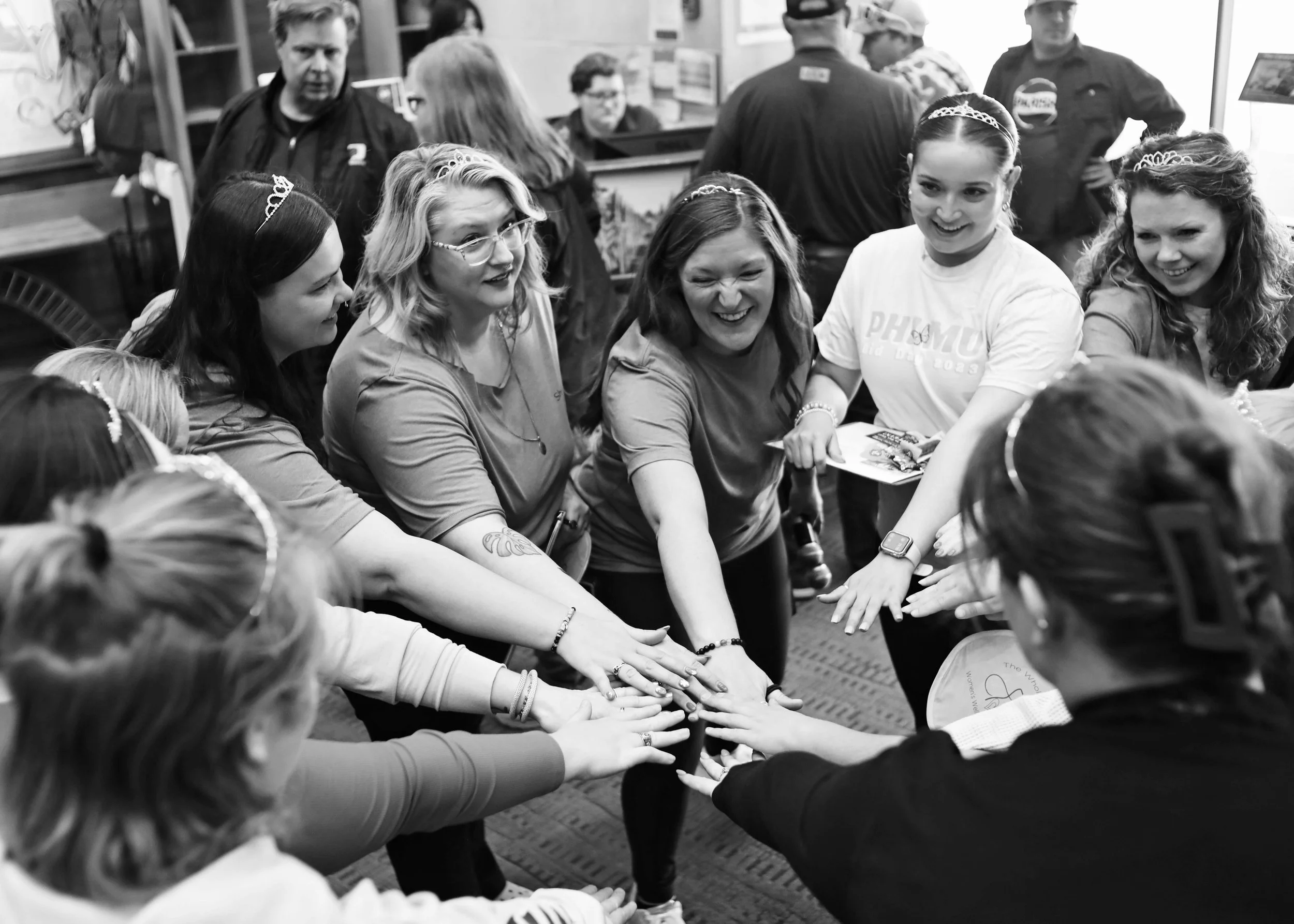 Group of women and girls in a circle with hands stacked in the center, smiling and celebrating in an indoor setting.