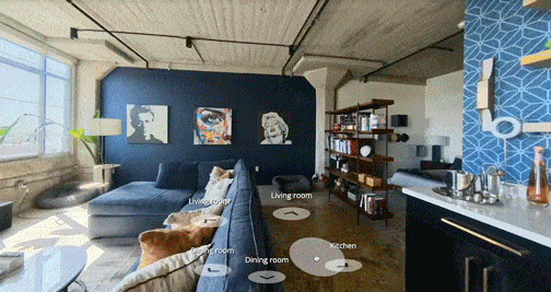 Living room with blue walls, artwork, a gray sectional sofa, a dog on the sofa, dining area, and kitchen with white countertops and dark cabinets.