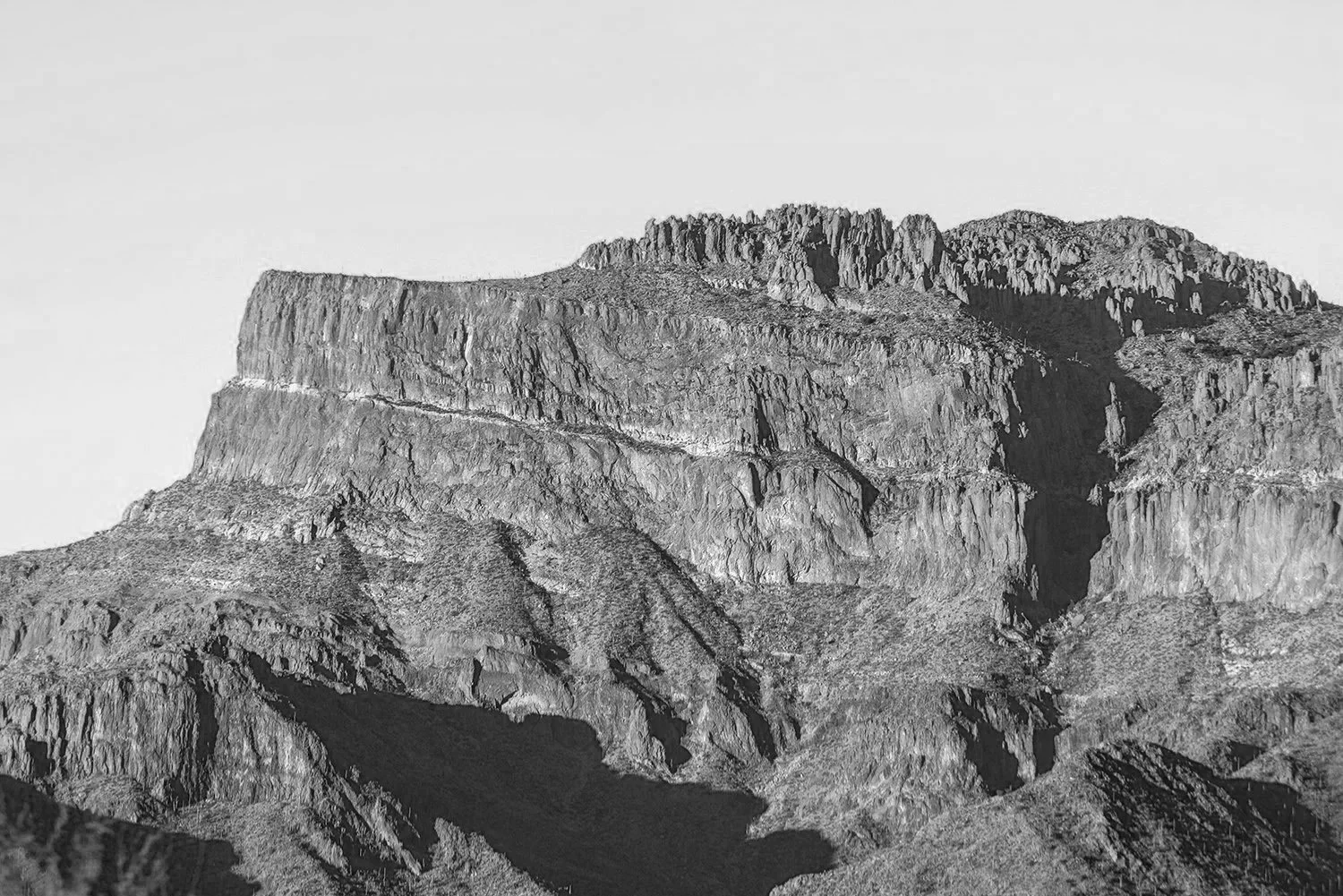 Black and white photograph of a rugged mountain with steep cliffs and jagged rock formations.
