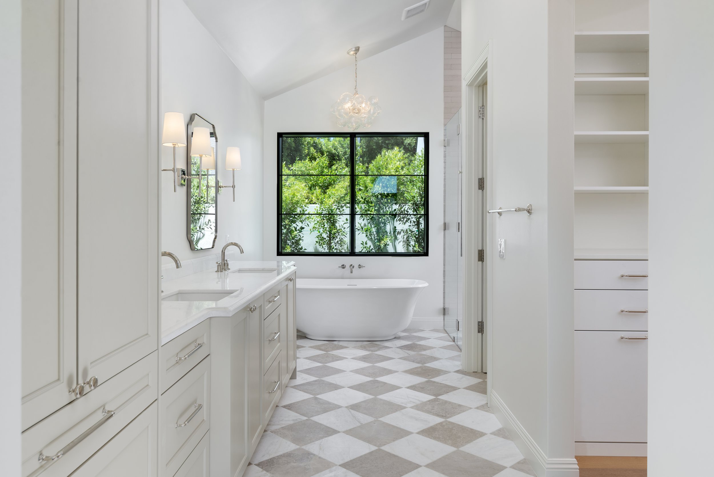 Bright and modern bathroom with a white bathtub, large window showing greenery outside, and white cabinetry.