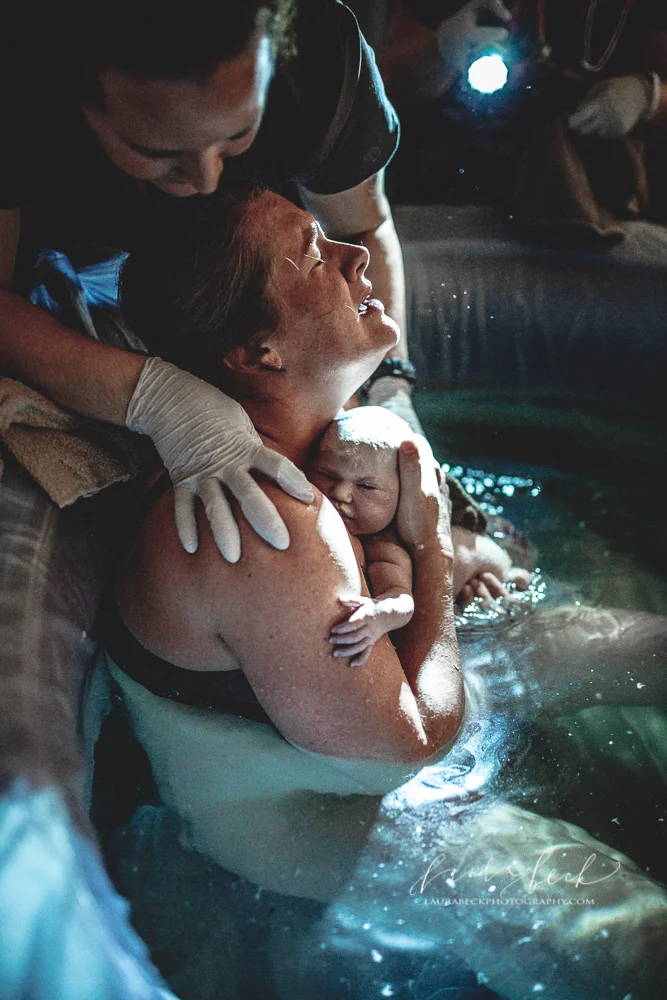 ​Mother holds her newborn baby right after giving birth in her birthing tub