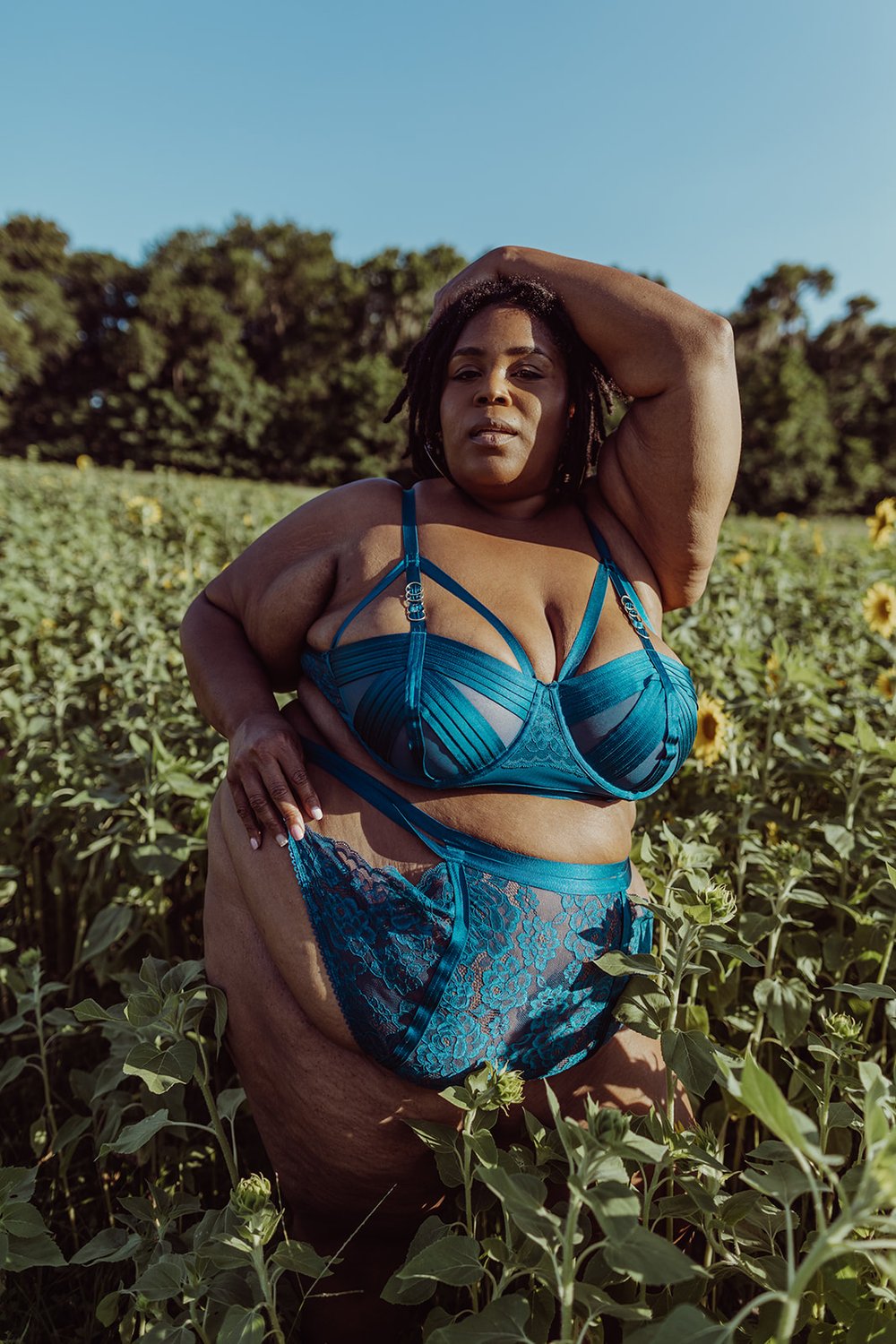  black woman looks into the camera while resting one arm above her head during her boudoir shoot in a sunflower field  