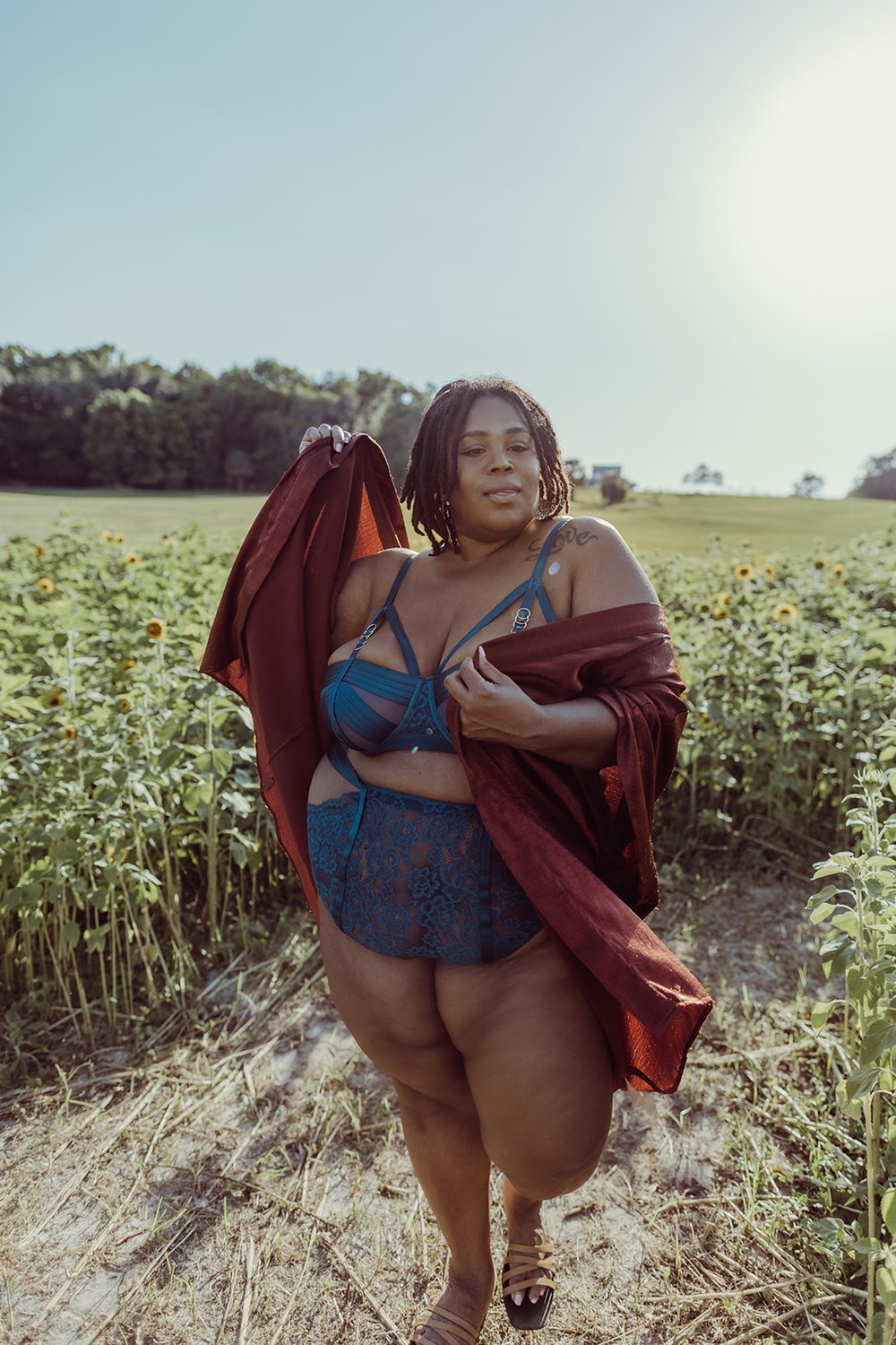  black woman walks barefoot in a sunflower field in blue lingerie and an orange coverup during her boudoir session in Florida 