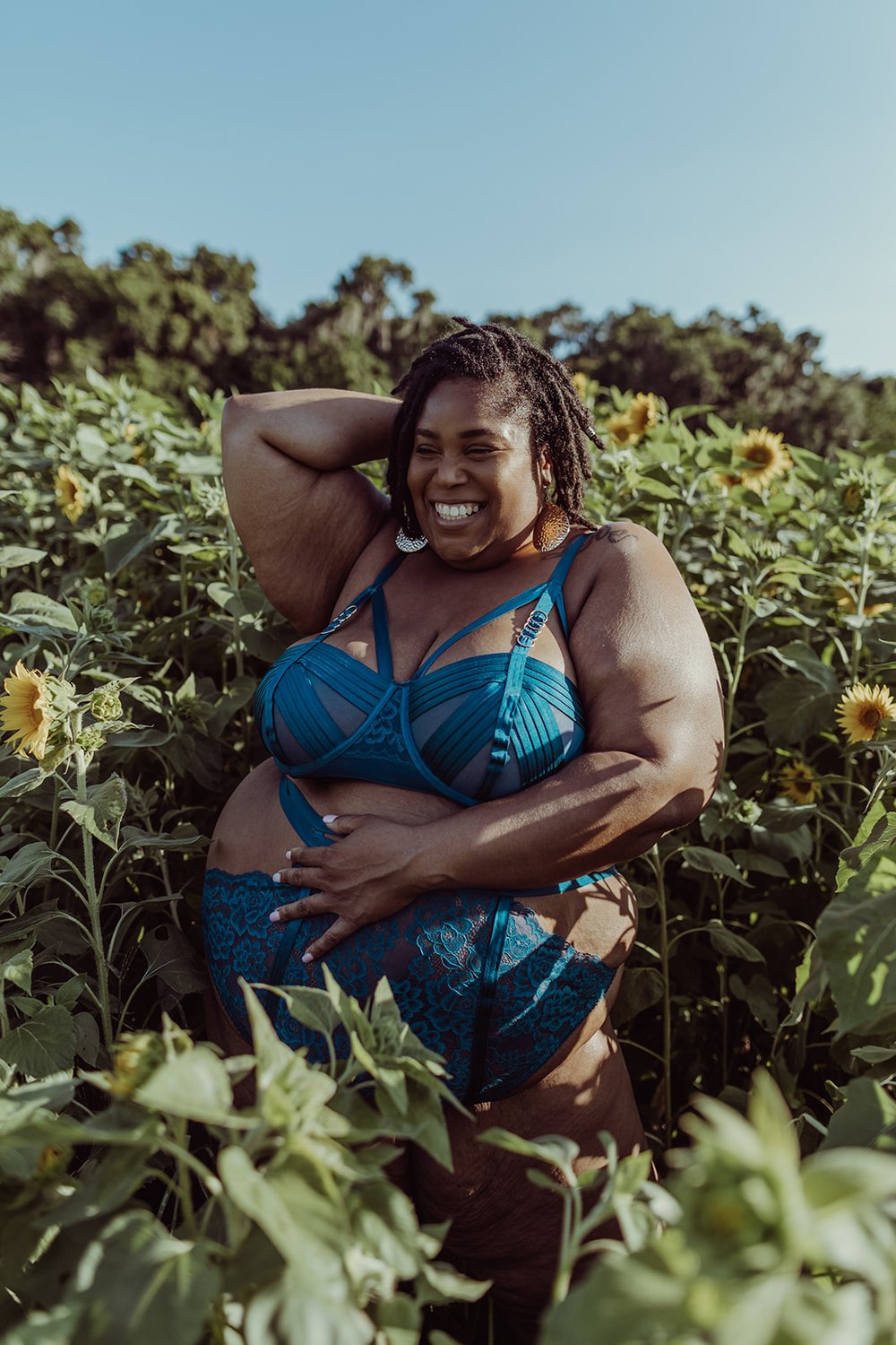  black woman smiling during her outdoor photoshoot in a sunflower field as her boudoir photographer captures the moment 