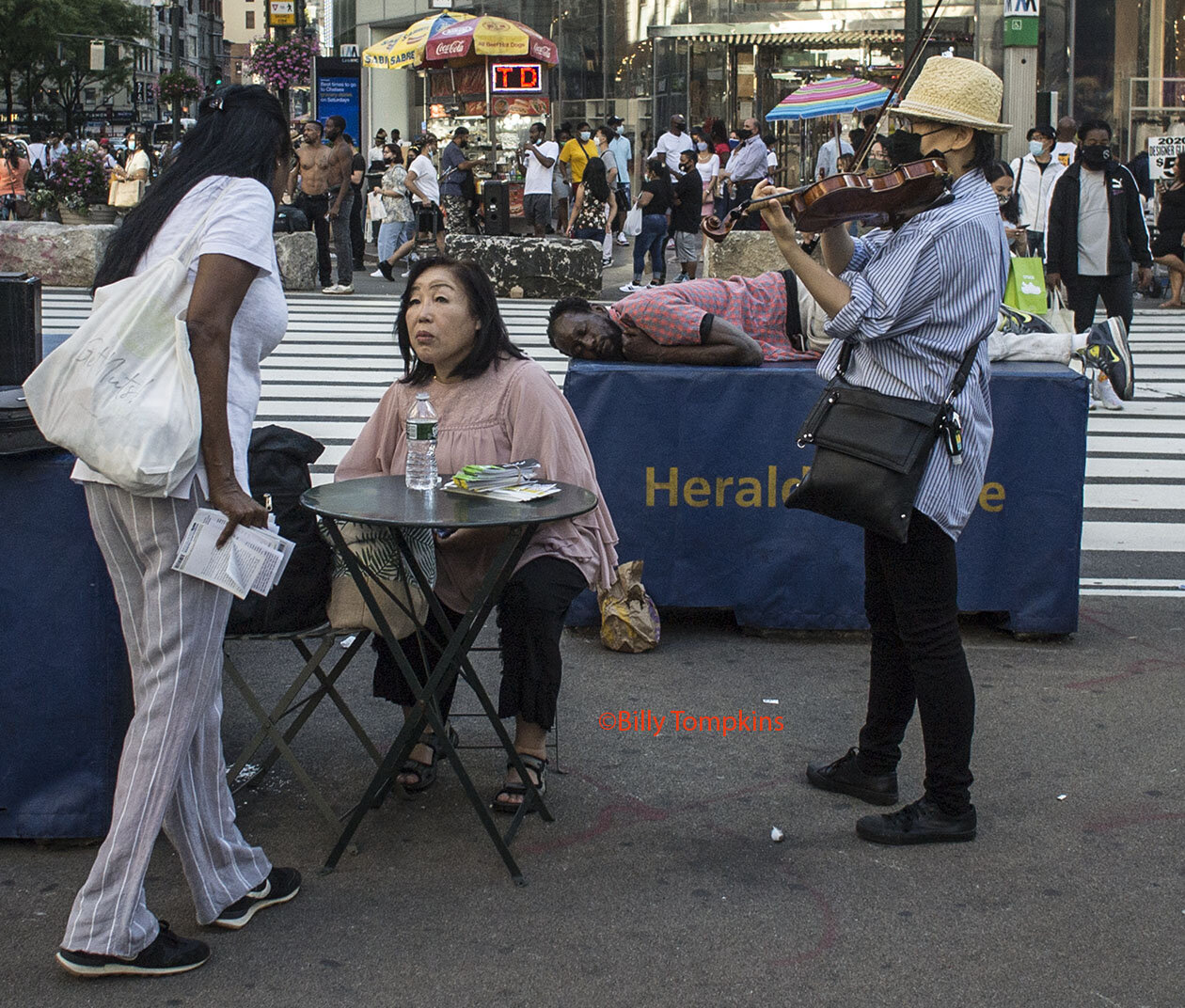  Fiddle player,  plays the fiddle  as  a woman tells   a seated woman  all about Jesus  as  a tired guy behind them   takes a much needed mid-afternoon nap.  34th street  2020  New York City 