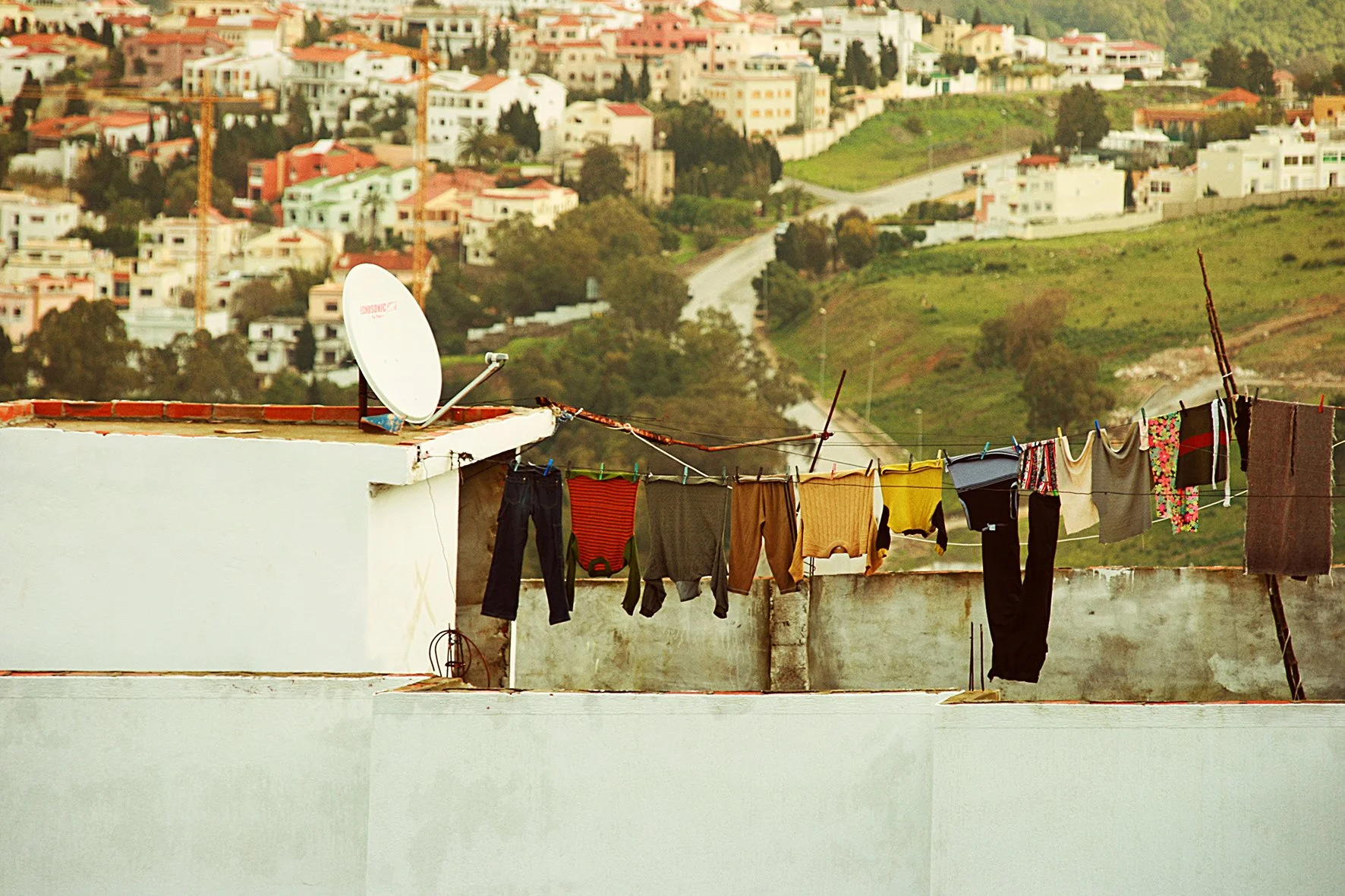 Vêtements suspendus à une corde à linge sur un toit avec vue sur une ville en pente et des collines verdoyantes en arrière-plan.
