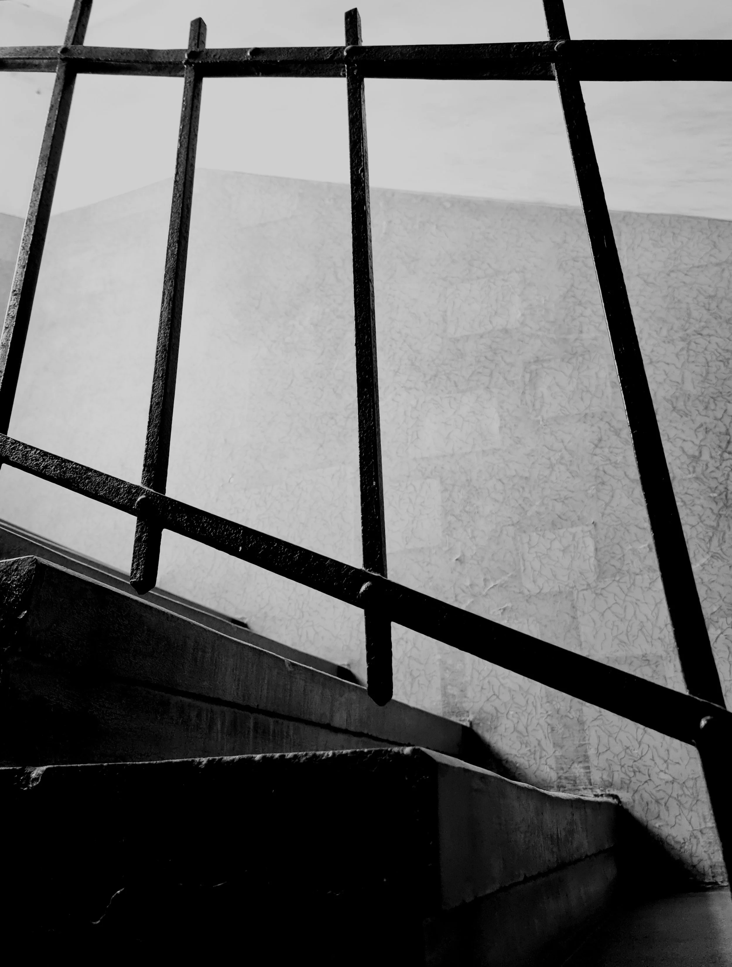 Vue en contre-plongée d'une rampe d'escalier en métal noir, avec un mur à fond blanc peint avec une texture craquelée.