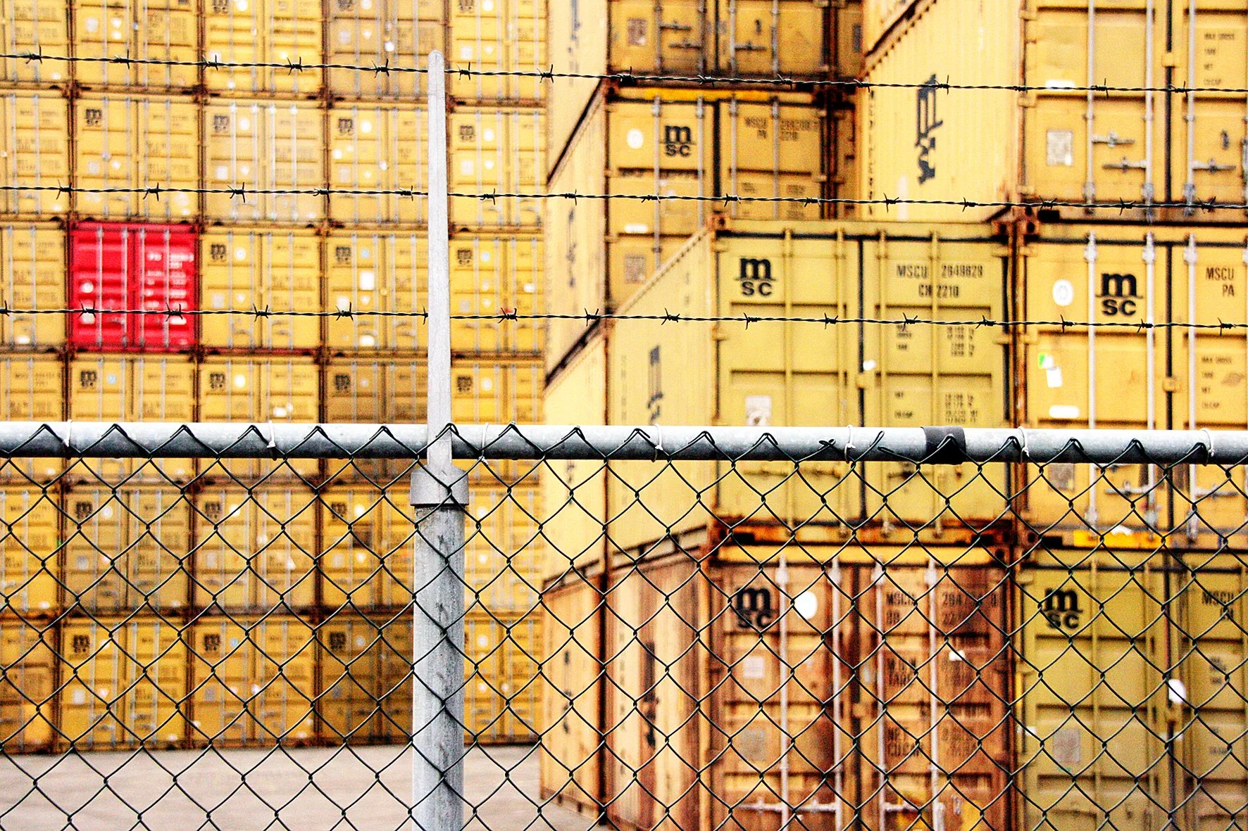Pile de conteneurs de stockage en couleur jaune et rouge derrière une clôture de fil de fer barbelé.