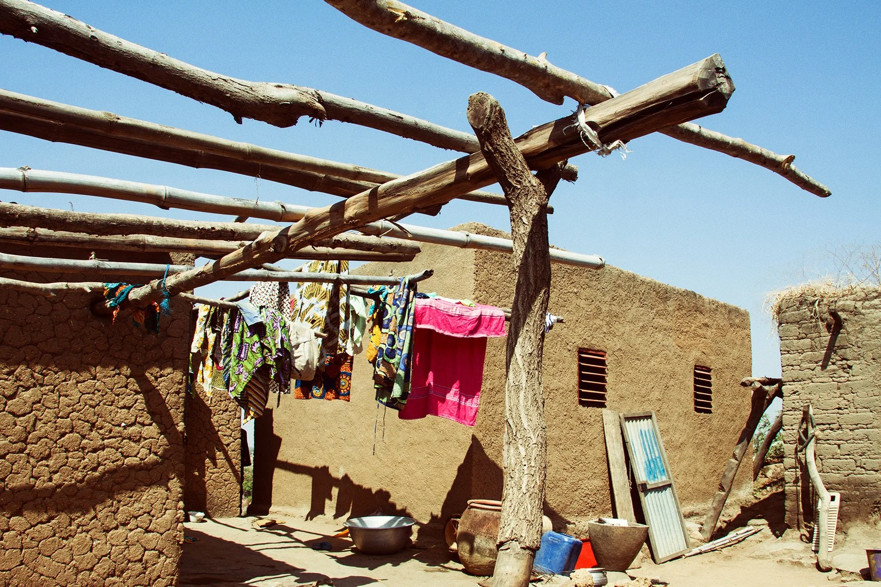 Vêtements suspendus pour sécher à l'extérieur d'une maison en terre dans un environnement rural, avec un ciel bleu en arrière-plan.