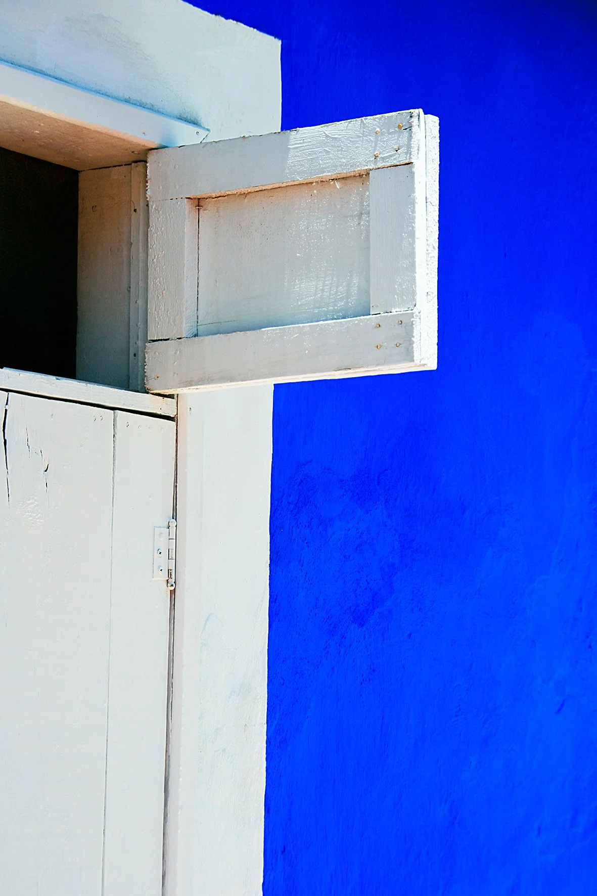 avant d'un mur bleu, une fenêtre blanche en bois avec volets fermés.