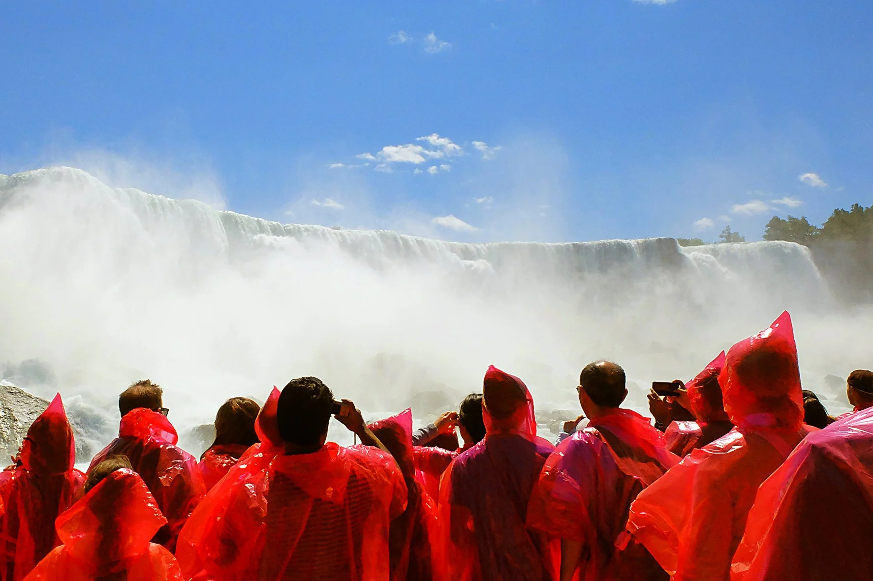 Groupe de personnes portant des ponchos rouges, regardant les chutes du Niagara sous un ciel bleu avec quelques nuages.
