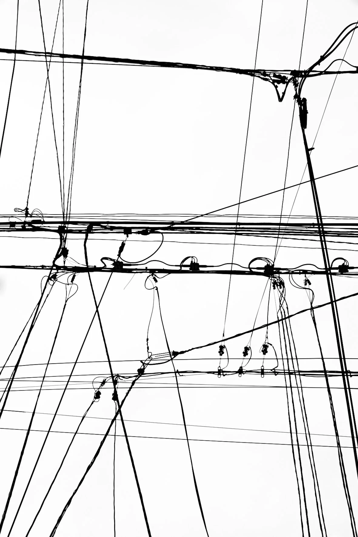 Câbles électriques noir et blanc vus de dessous, formant un réseau complexe contre le ciel blanc.