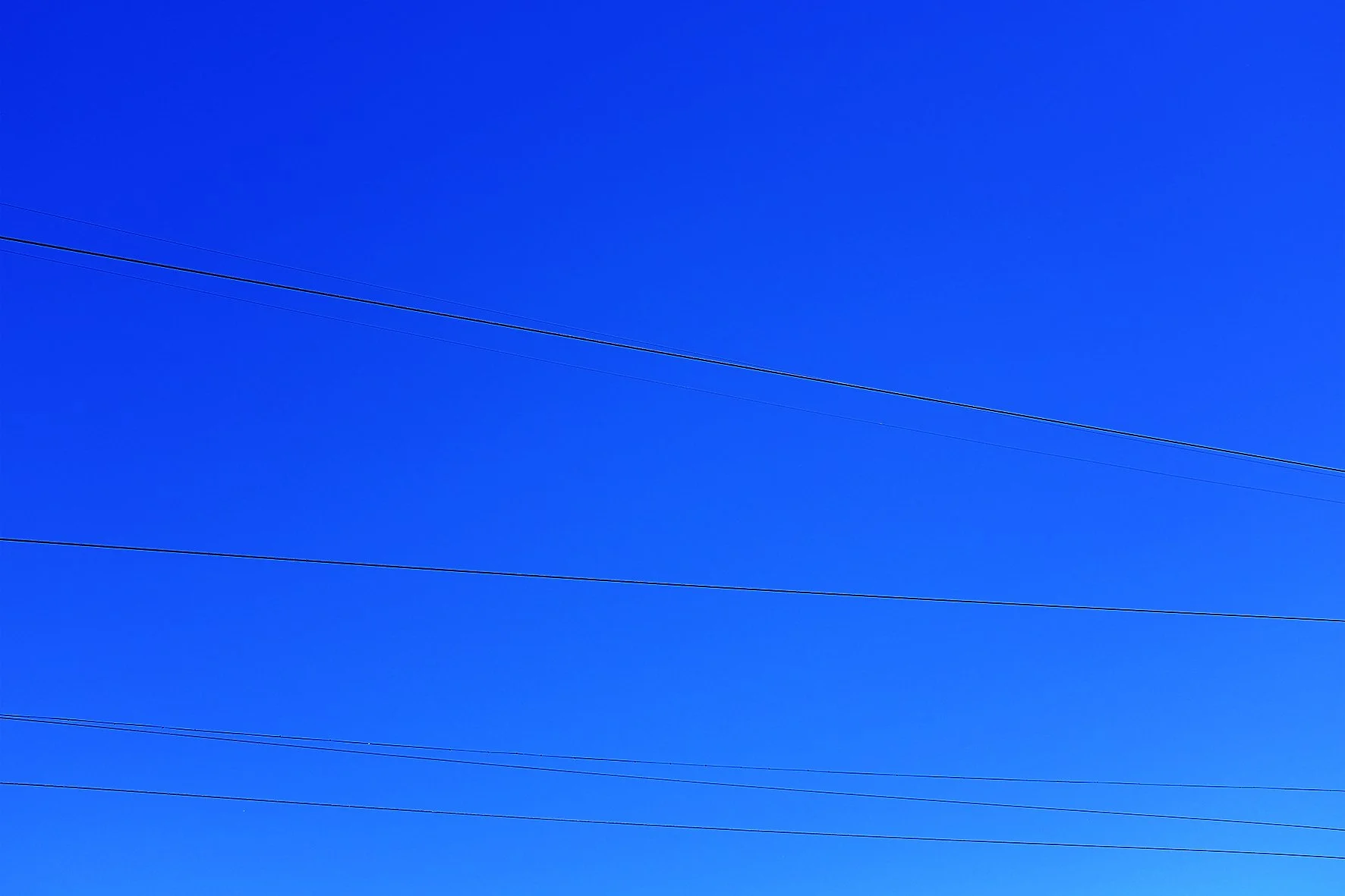 Ciel bleu clair avec plusieurs lignes électriques traversant l'image horizontalement.