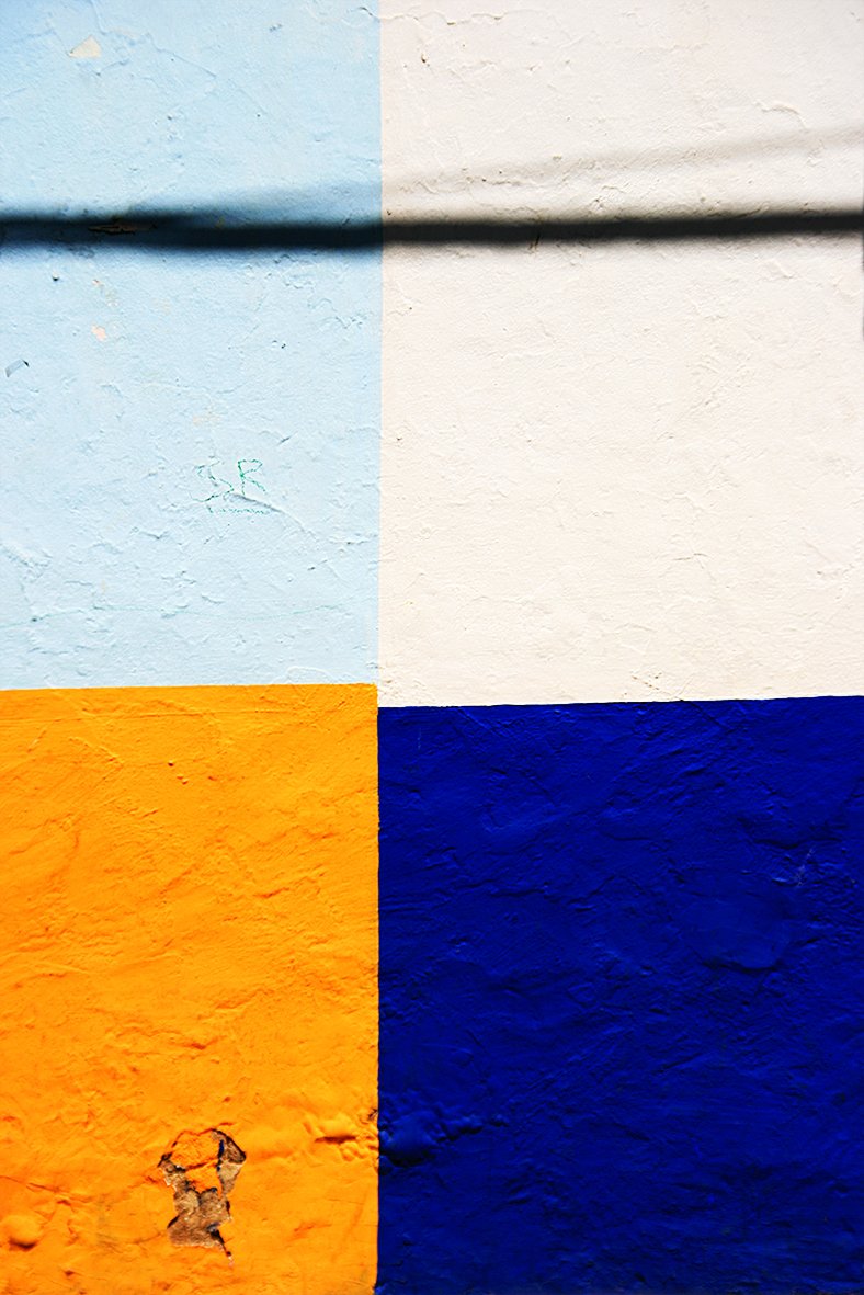 Mur divisé en quatre sections de couleurs différentes : bleu clair en haut à gauche, blanc en haut à droite, orange en bas à gauche, bleu foncé en bas à droite, avec une ombre passant horizontalement au centre.
