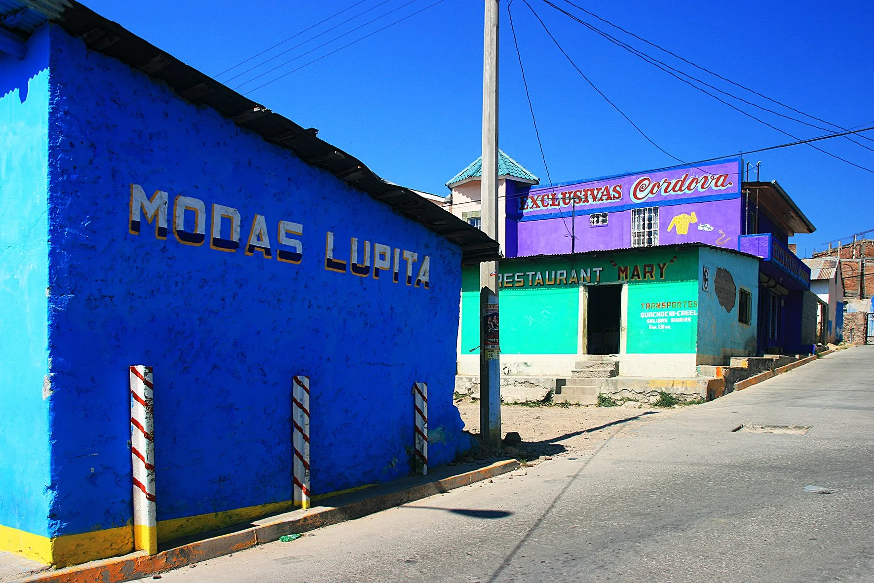 Rue avec maisons colorées, enseignes de restaurant et de boutique, ciel bleu clair, sans personnes visibles.