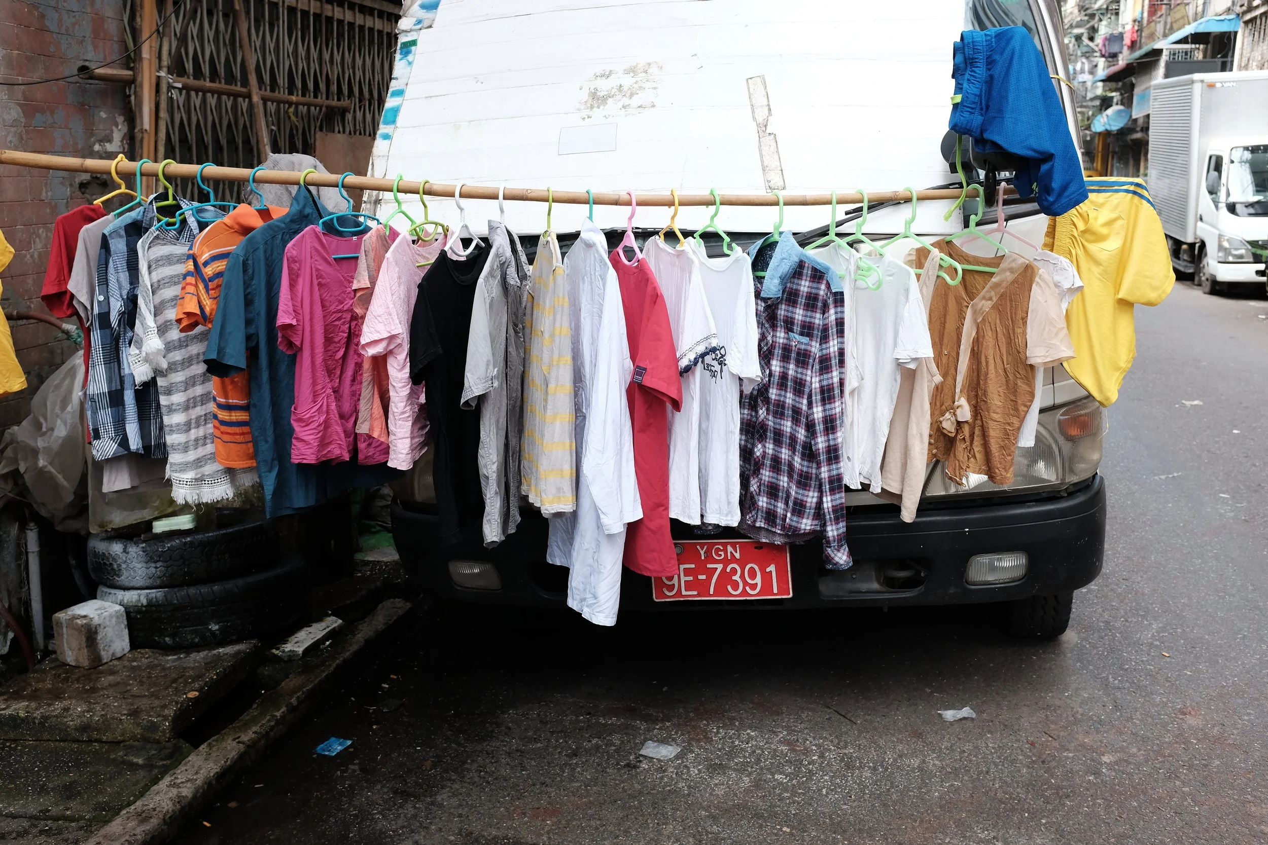 Vêtements variés suspendus sur une corde et accrochant à un véhicule dans une rue urbaine.