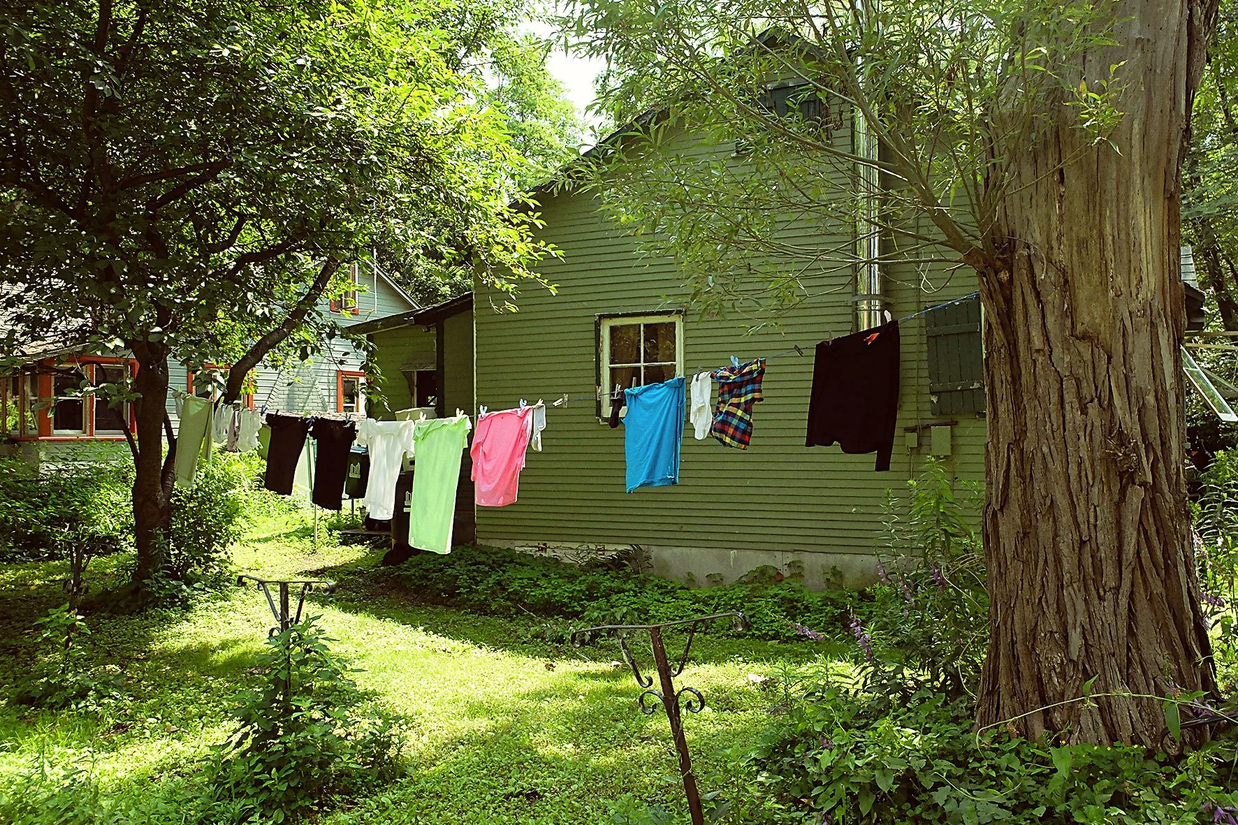 Linge suspendu à une corde à linge dans un jardin verdoyant avec une maison en fond.
