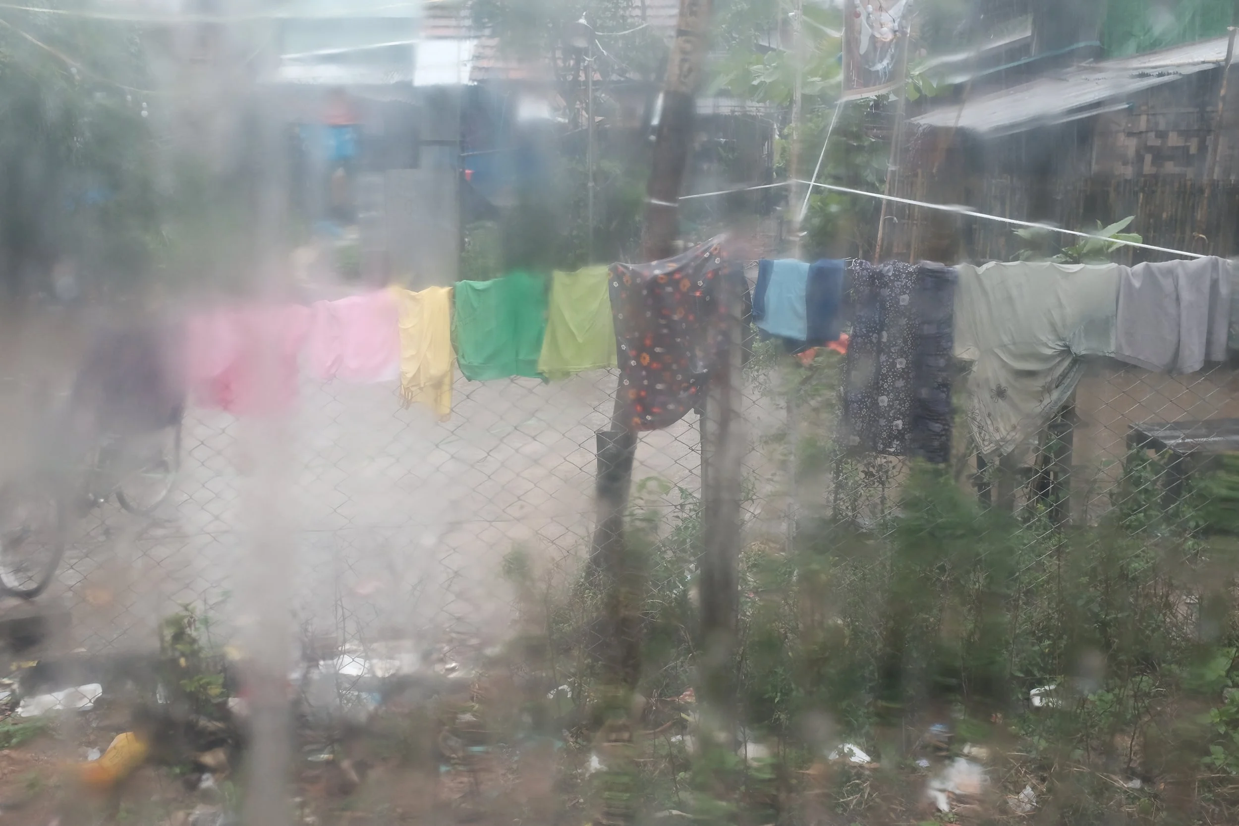 Vêtements suspendus pour sécher derrière une clôture en fil de fer dans une maison modeste, vue à travers une vitre embuée ou sale.