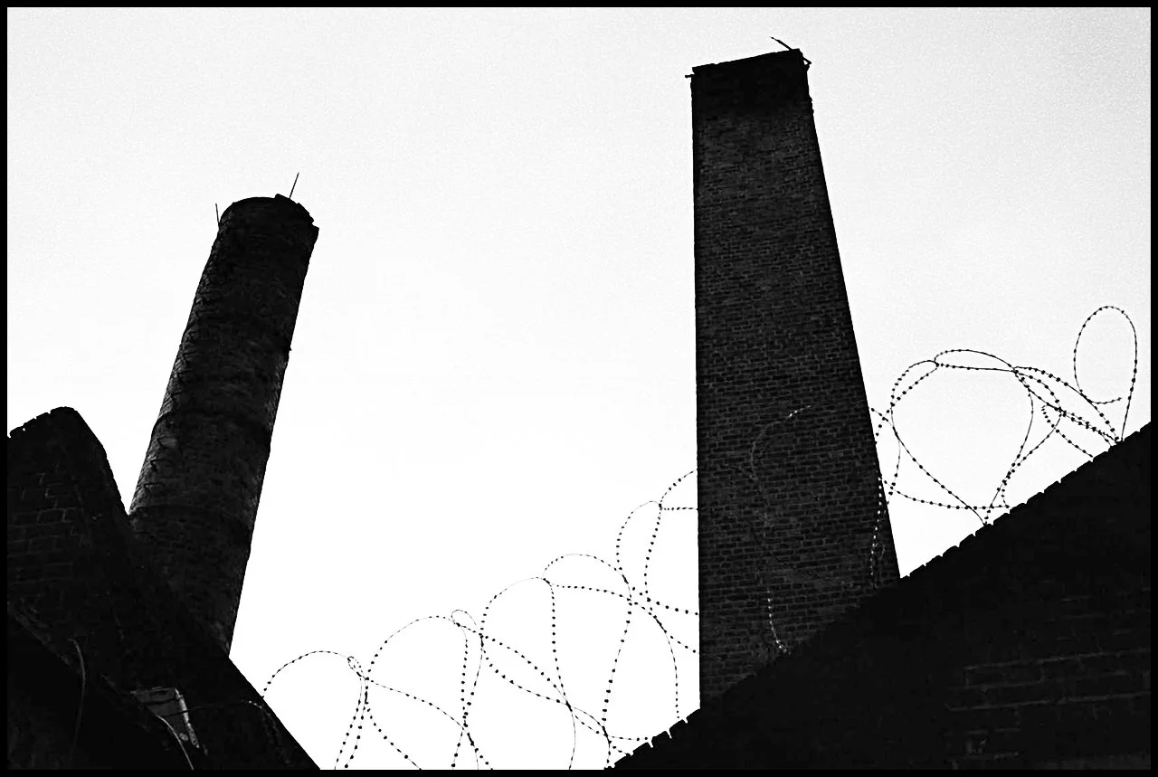 Deux cheminées en briques avec des fils barbelés autour d'elles vues en contre-jour.
