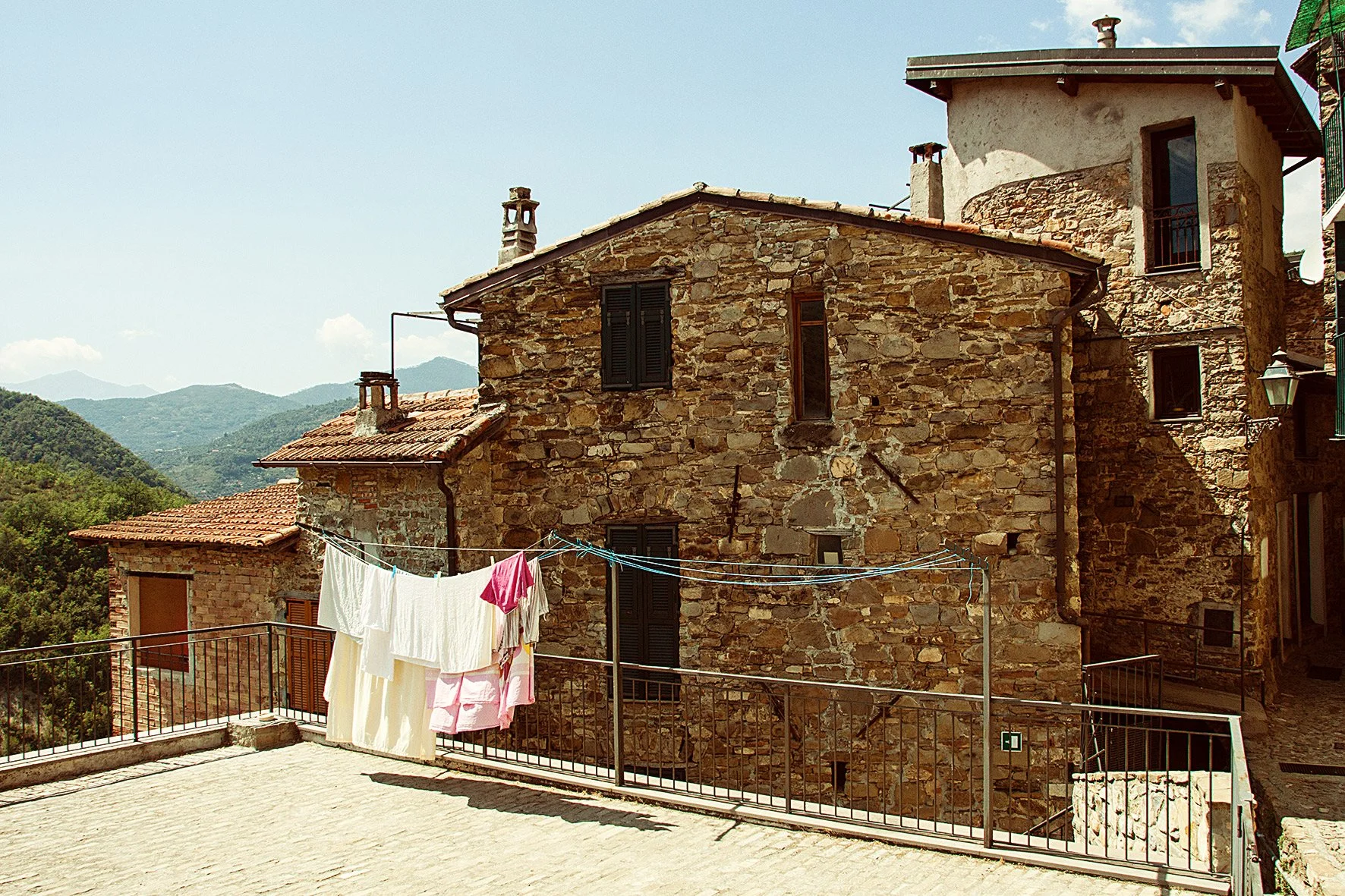 Maisons en pierre traditionnelles dans un village de montagne avec des montagnes en arrière-plan et du linge suspendu sur une corde à linge.