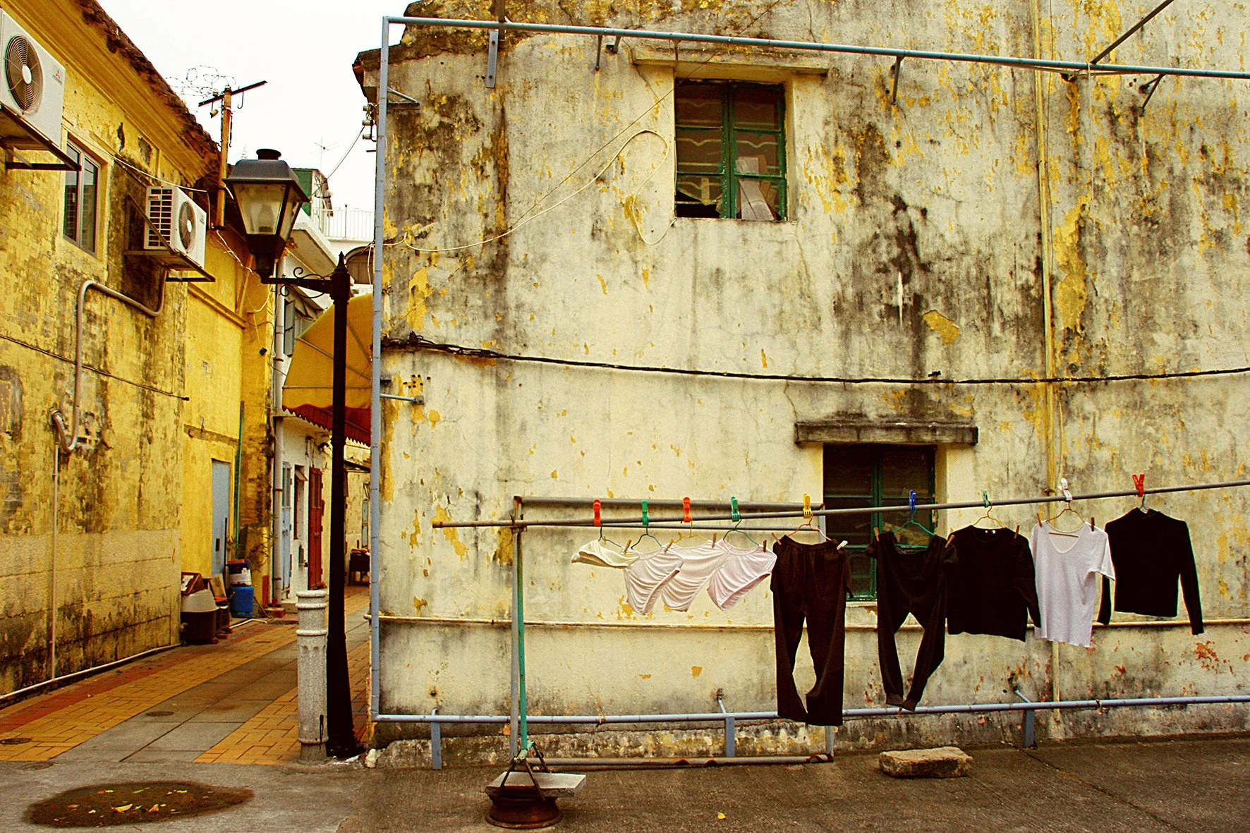Vêtements à sécher sur une corde à linge dans une vieille rue avec bâtiments usés et murs peints en jaune et blanc