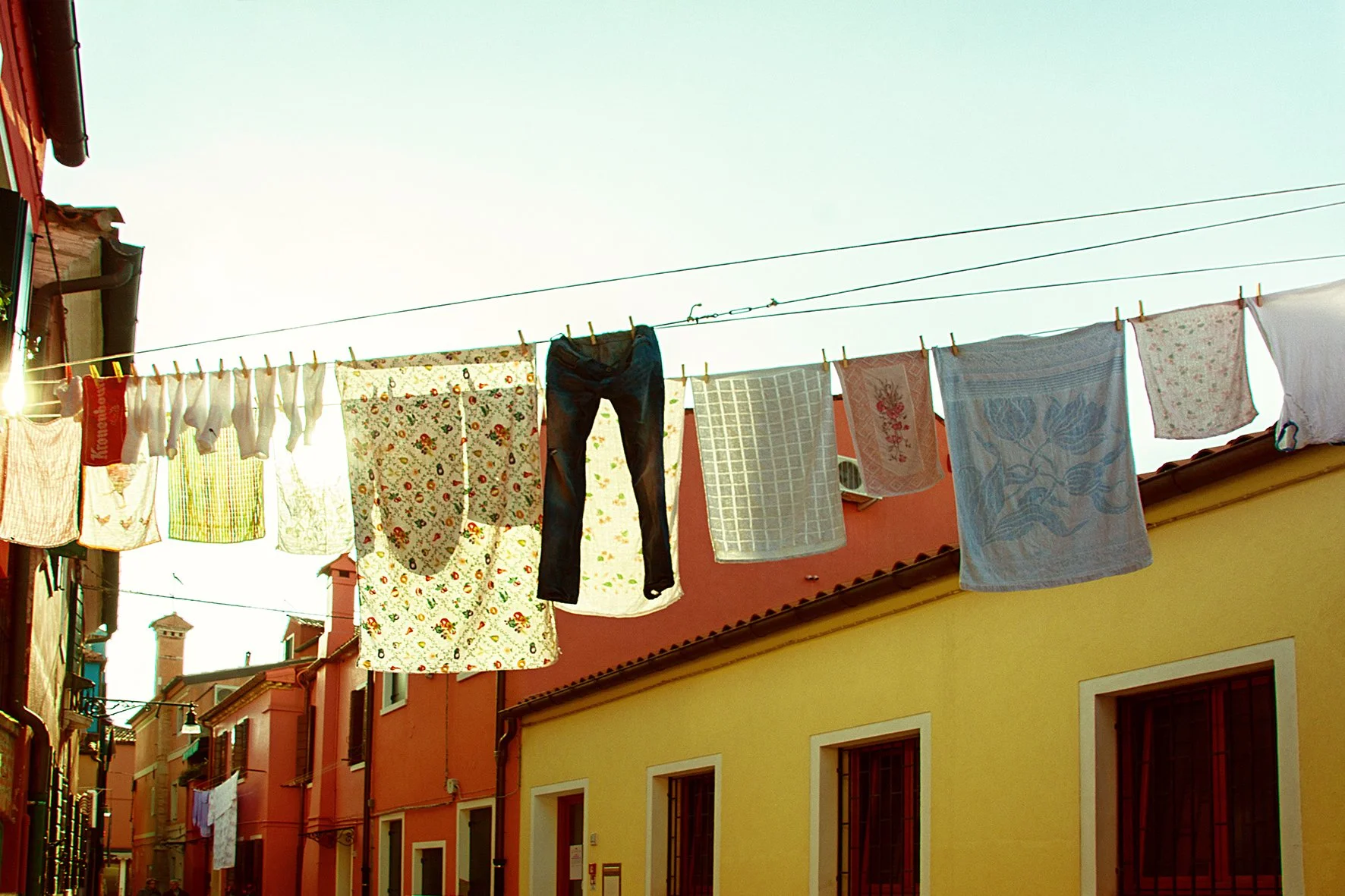 Linge à linge suspendu sur une corde dans une rue colorée, avec des bâtiments jaunes et rouges en arrière-plan, sous un ciel clair.