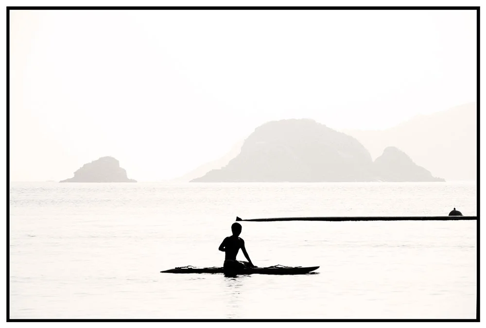 Silhouette d'une personne à cheval sur un paddleboard dans une mer calme avec des îles en arrière-plan, en noir et blanc.