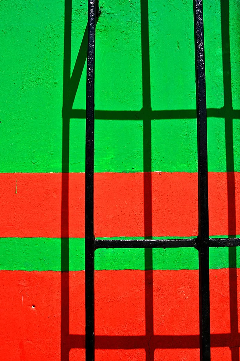 Barreaux noirs sur un mur peint en vert et rouge avec des ombres portées des barreaux.