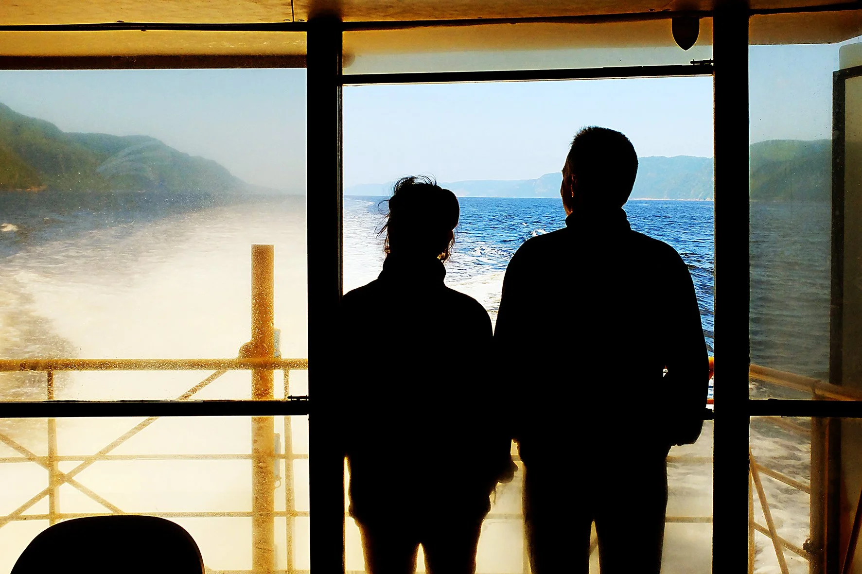 Silhouettes de deux personnes regardant la mer depuis une fenêtre de bateau.