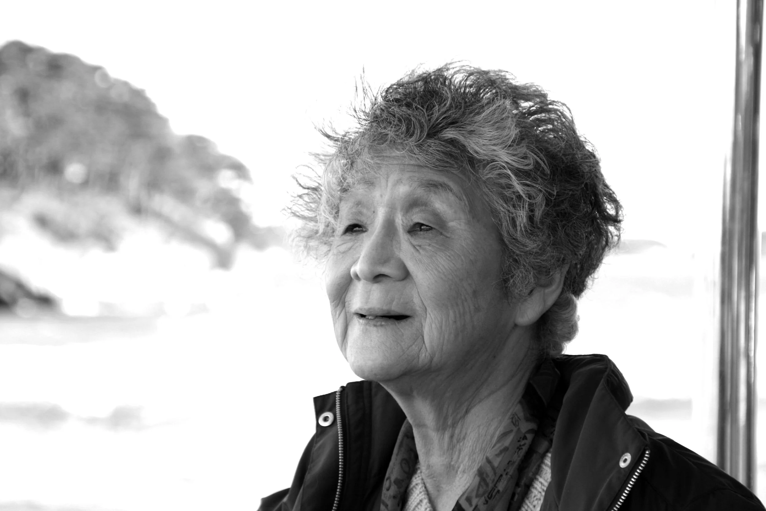 Femme âgée avec des cheveux bouclés et gris, portant un manteau et un foulard, en plein air