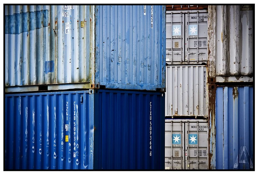 Multiple conteneurs de stockage maritime empilés, principalement en bleu et gris, avec des marques Maersk et des codes d'identification.