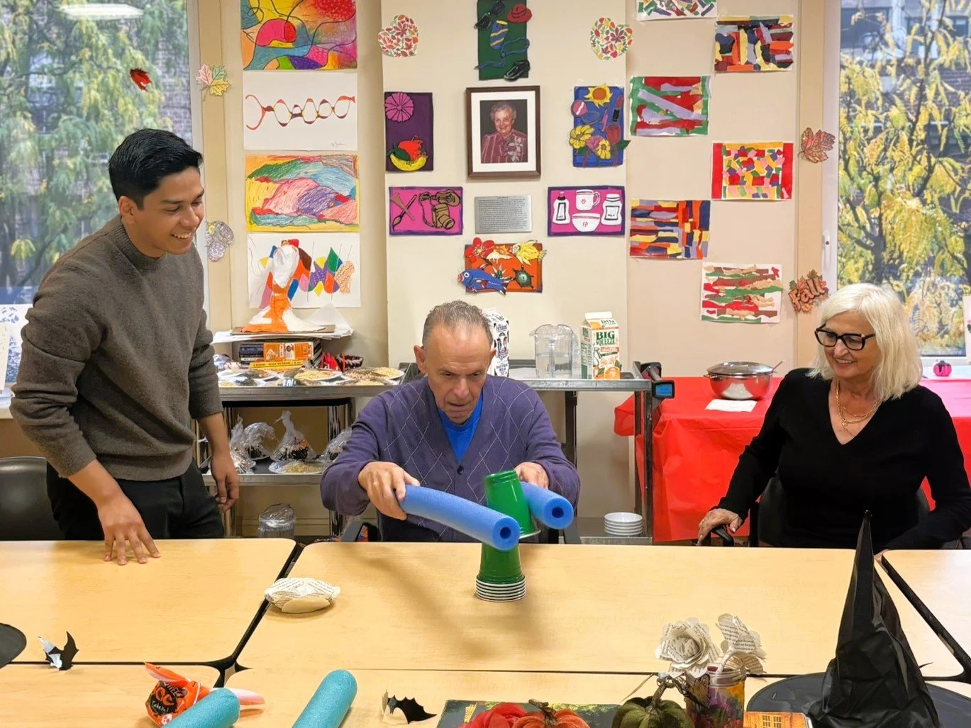photo showing older adult using two pool floation noodles to pick up a green plastic cup