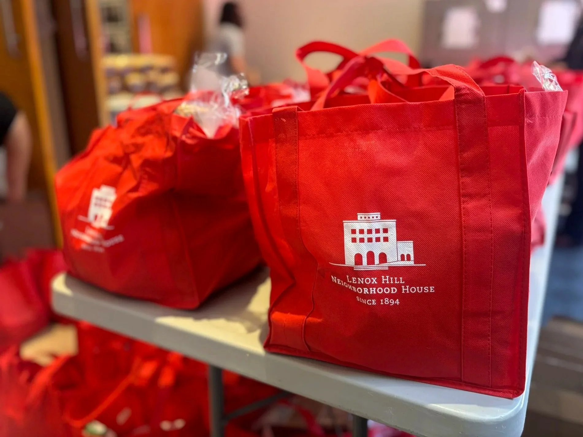 red cloth bags, filled with food, on table with lenox hill neighborhood house logo in white