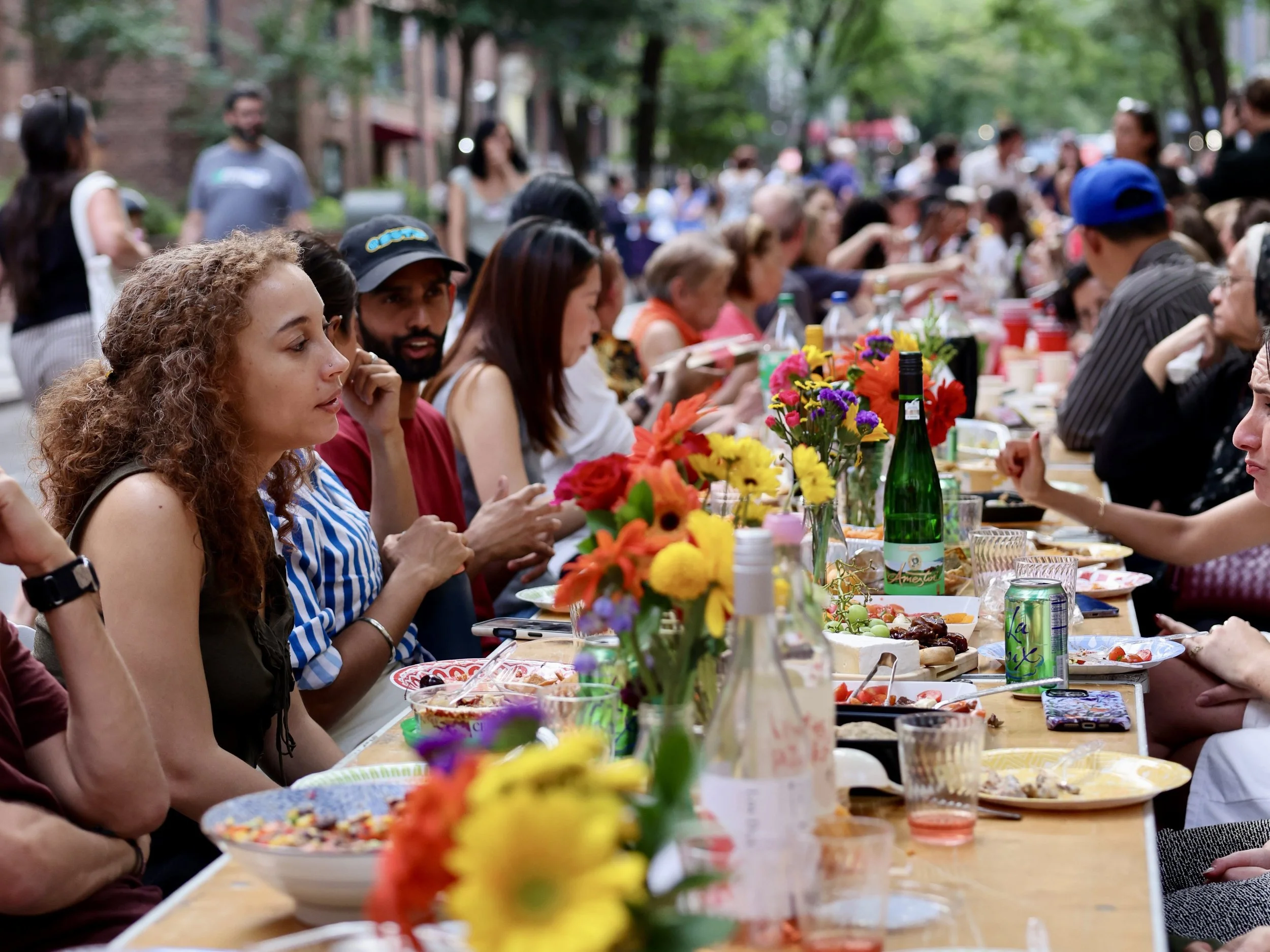 photo showing neighbors sitting across from one another at a table filled with colorful flowers and plates of food