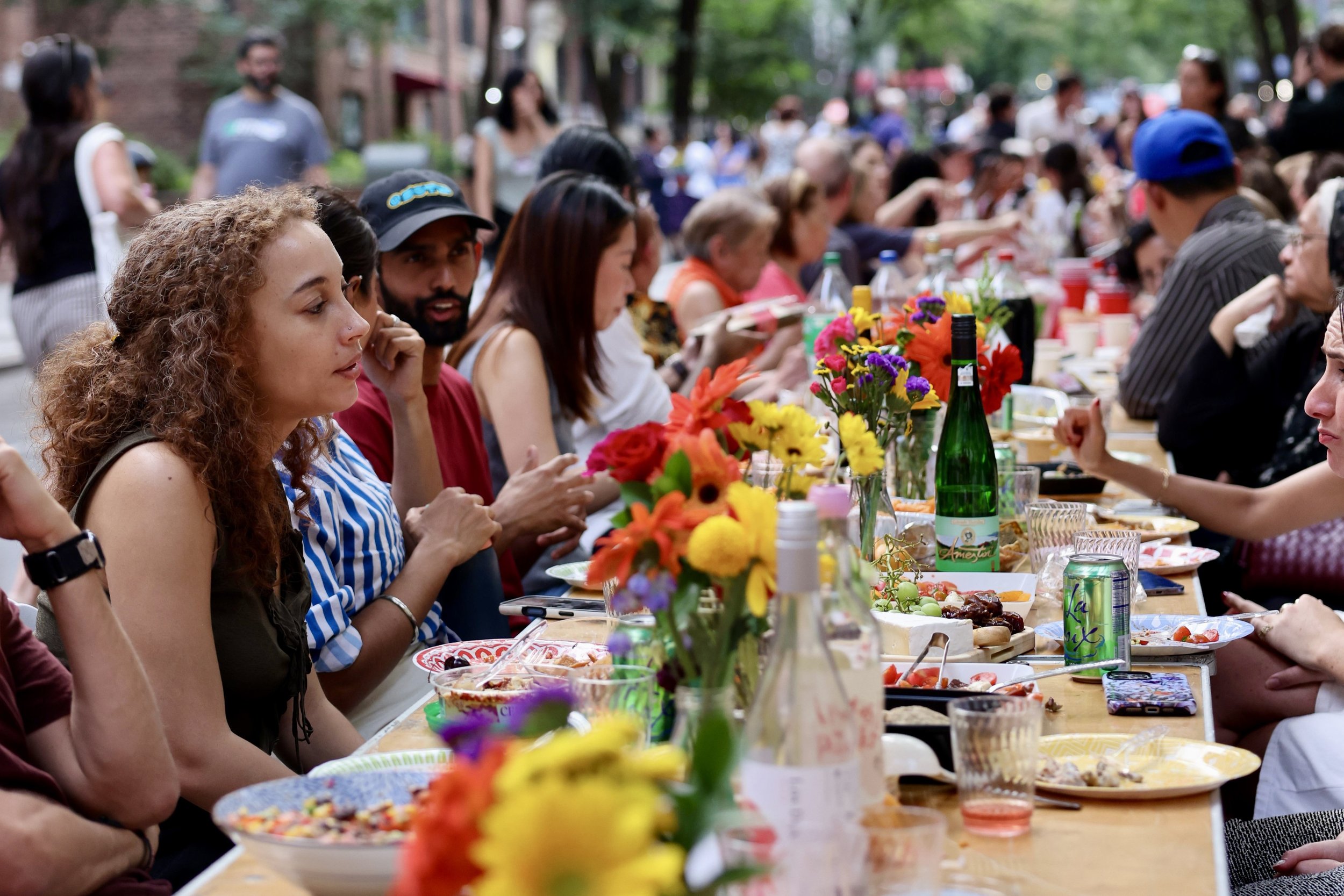 photo of hundreds of neighbors of all ages sitting at a long table sharing a meal outdoors