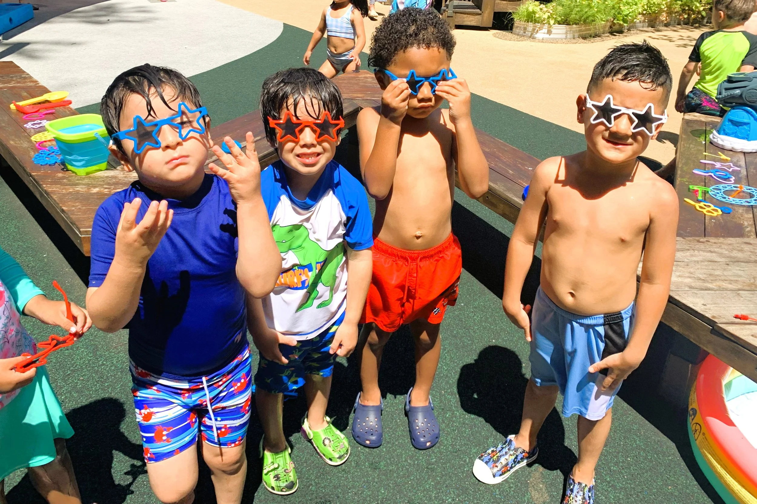 four young children wearing star-shaped sunglasses outdoors in colorful swimming gear