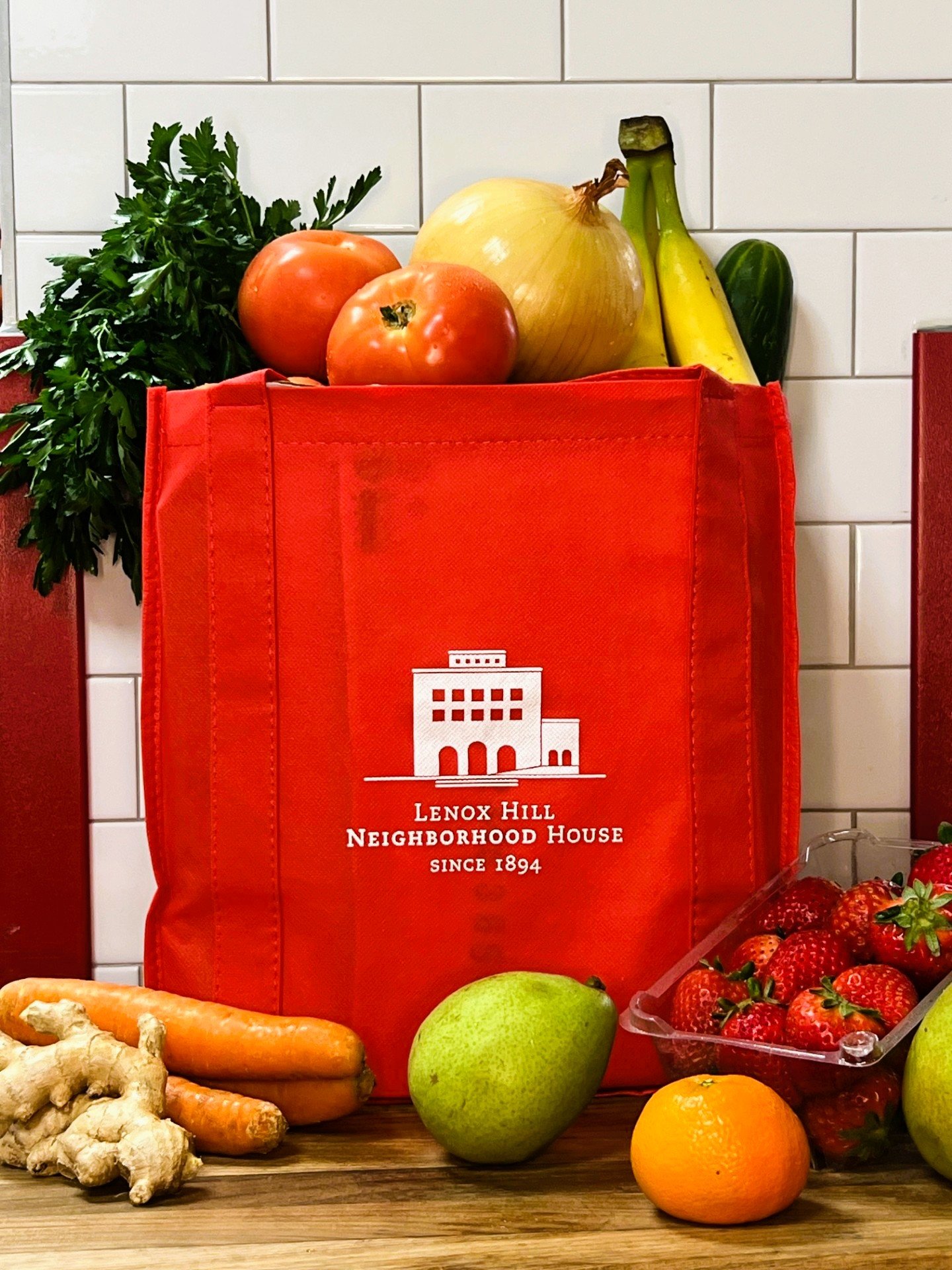 red bag with Lenox Hill Neighborhood House logo on top of a wooden countertop filled with fresh produce