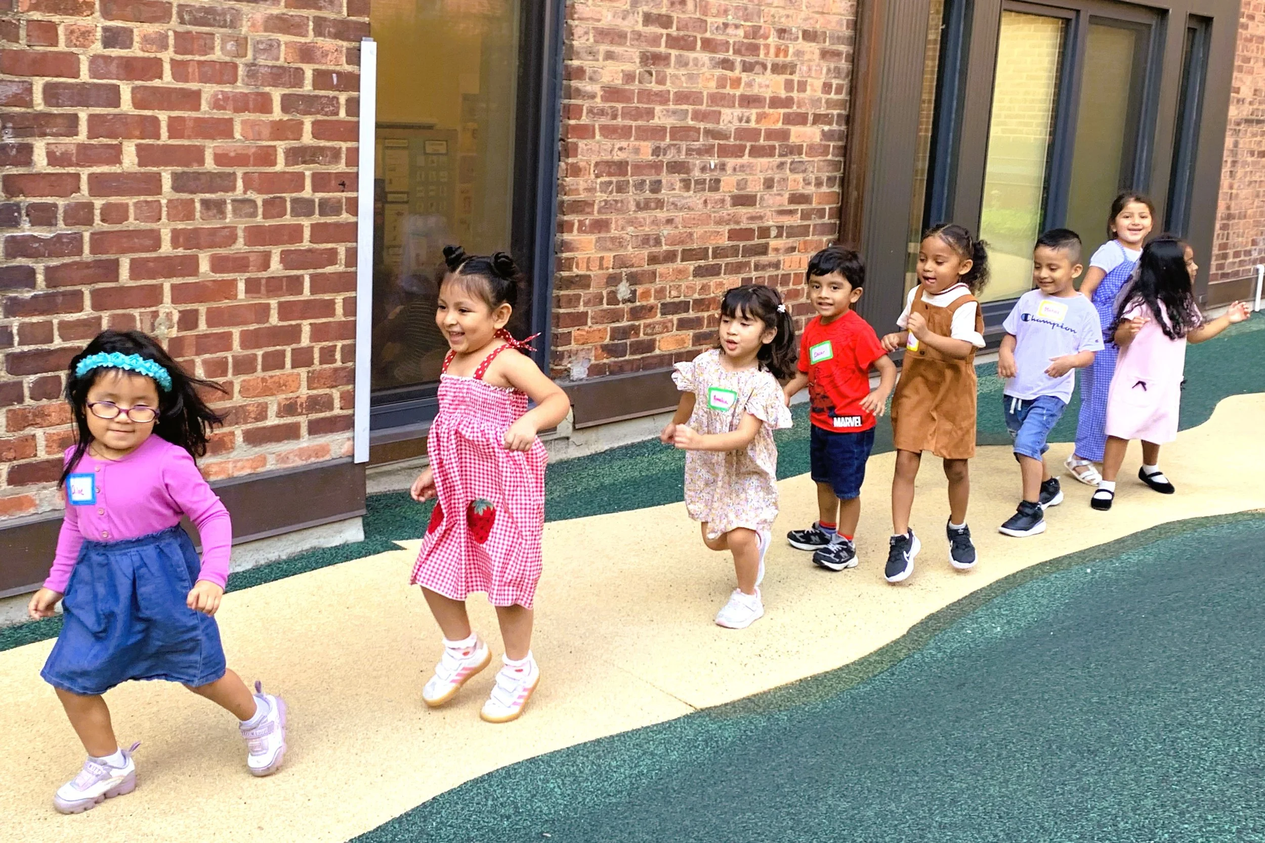 photo of eight preschoolers running outdoors near a brick building
