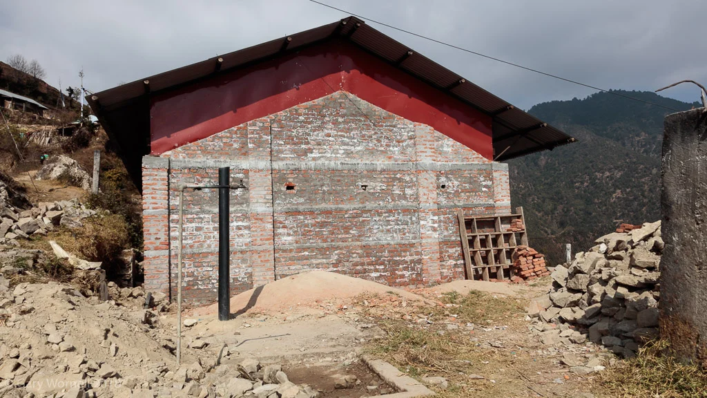 Rubble from the old school fills the yard outside the new school building. A drain pipe rises above the ground where the new toilet will be. 