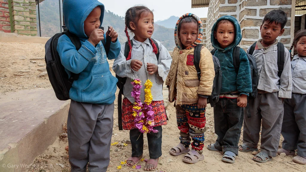 A young girl standing in line with her classmates holds a garland of wild flowers after receiving her bag.