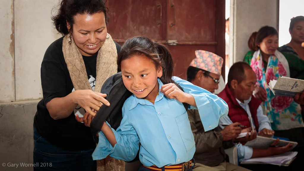 Founder of Moving Mountain Nepal Rewati Gurung helps a young student on with her new school bag.