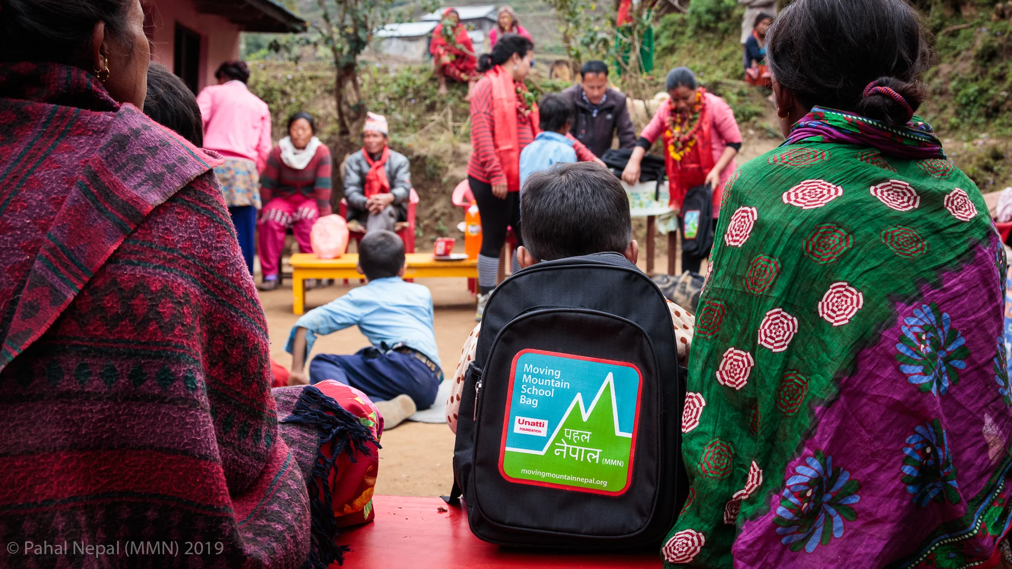 A young student sits on a bench beside his mother as the bag donation program continues at Bhumistan Basic School in Dhading.