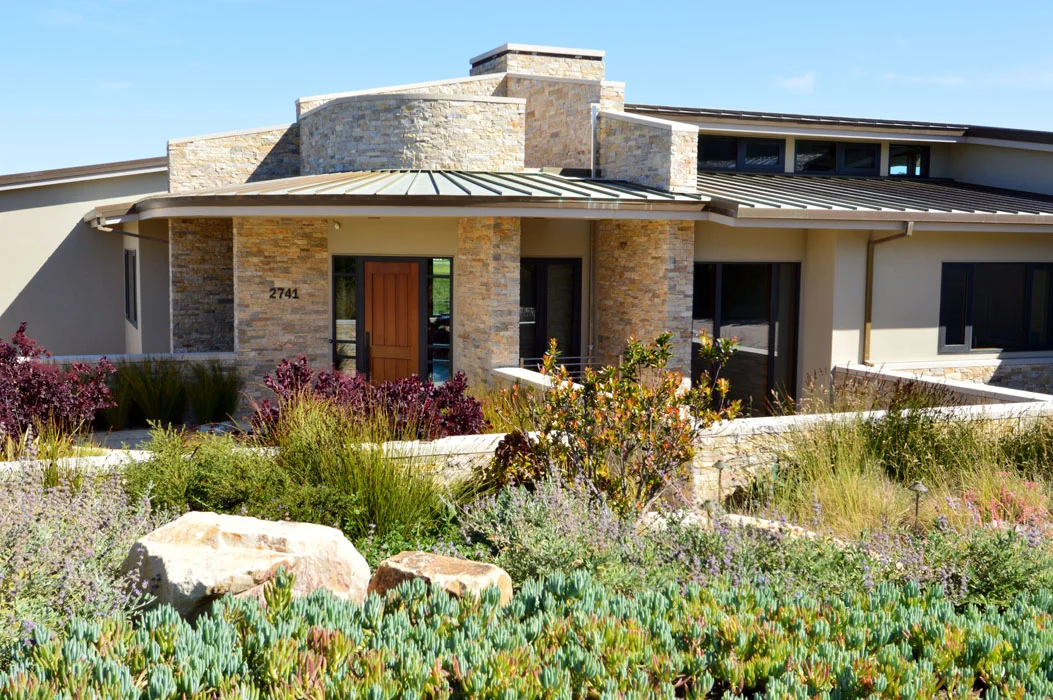 Carmel / The owners of this new home, perched on the edge of a slope overlooking the Pacific Ocean and Carmel River, wanted a low-maintenance landscape that reflected and merged seamlessly with the surrounding views and context. The slope, once inhabited by invasive species such as bamboo, required extensive erosion control stabilization and hillside restoration plantings to enhance the riparian zone. The new native plant mix effectively frames the dramatic, ever-changing river views and provides privacy screening. JLJA also designed the formal entry from street and driveway, incorporating swaths of low maintenance, native or regionally-adapted species to both set off the stone paving and low walls and provide strategic screening. Highlights of the home are two sunken courtyards that serve as light wells; with decorative gravel on the ground, they feature custom corten planters holding striking 'Sango-kaku' Japanese maples.