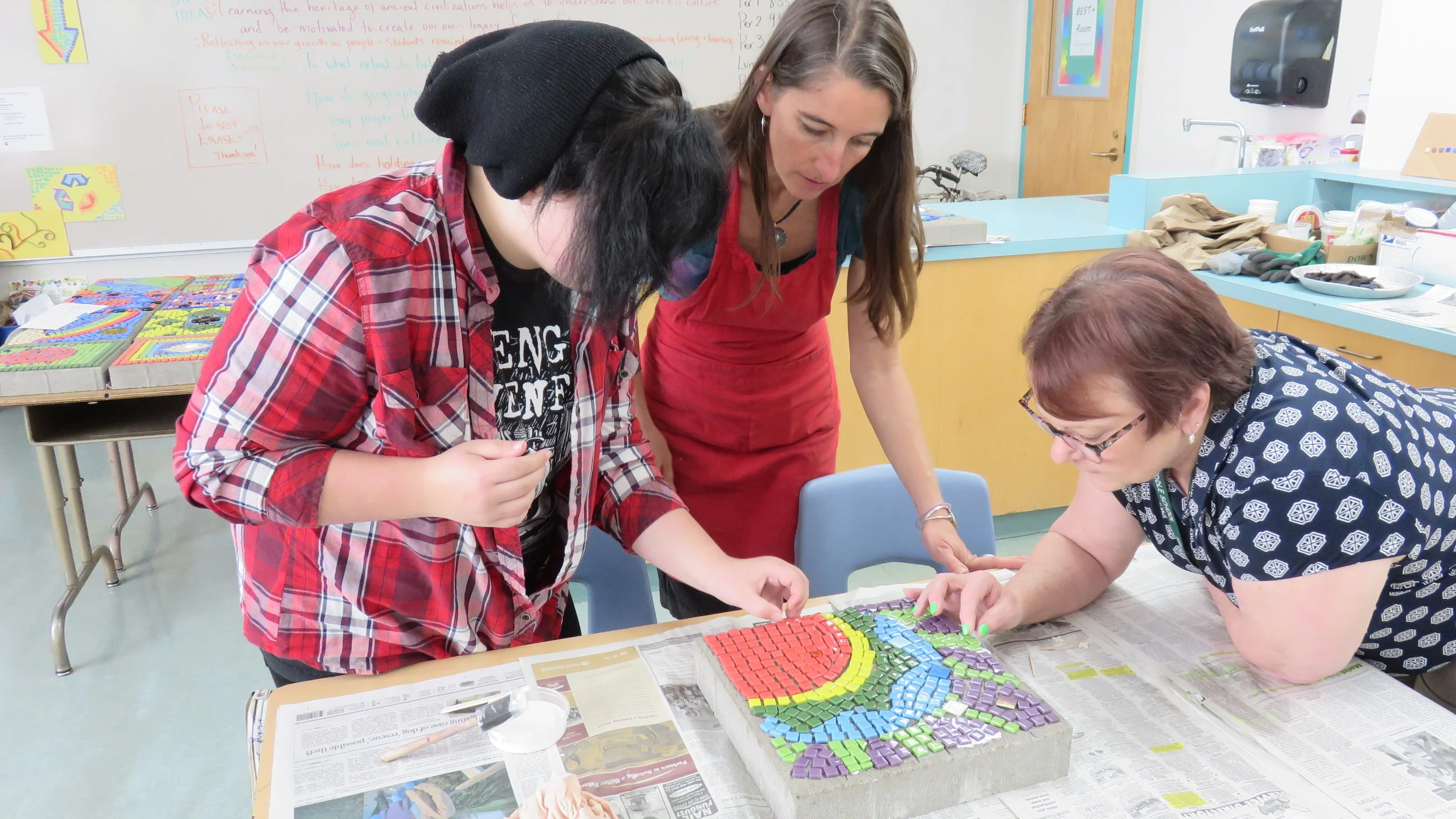 Kelly Middle School student, ArtCore weaver Jessica Land, and teacher Barb Whitlock discuss the mosaic design project inspired by a social studies unit on ancient civilizations. 