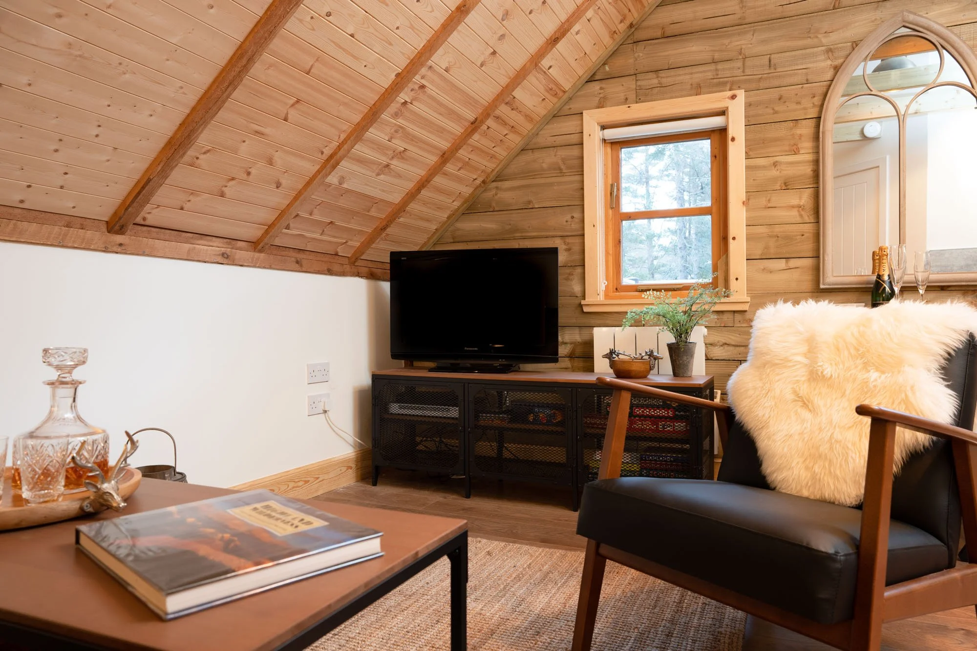 Scandinavian barn style iving area at The Hayloft with television, armchair and warm timber-clad vaulted ceiling.