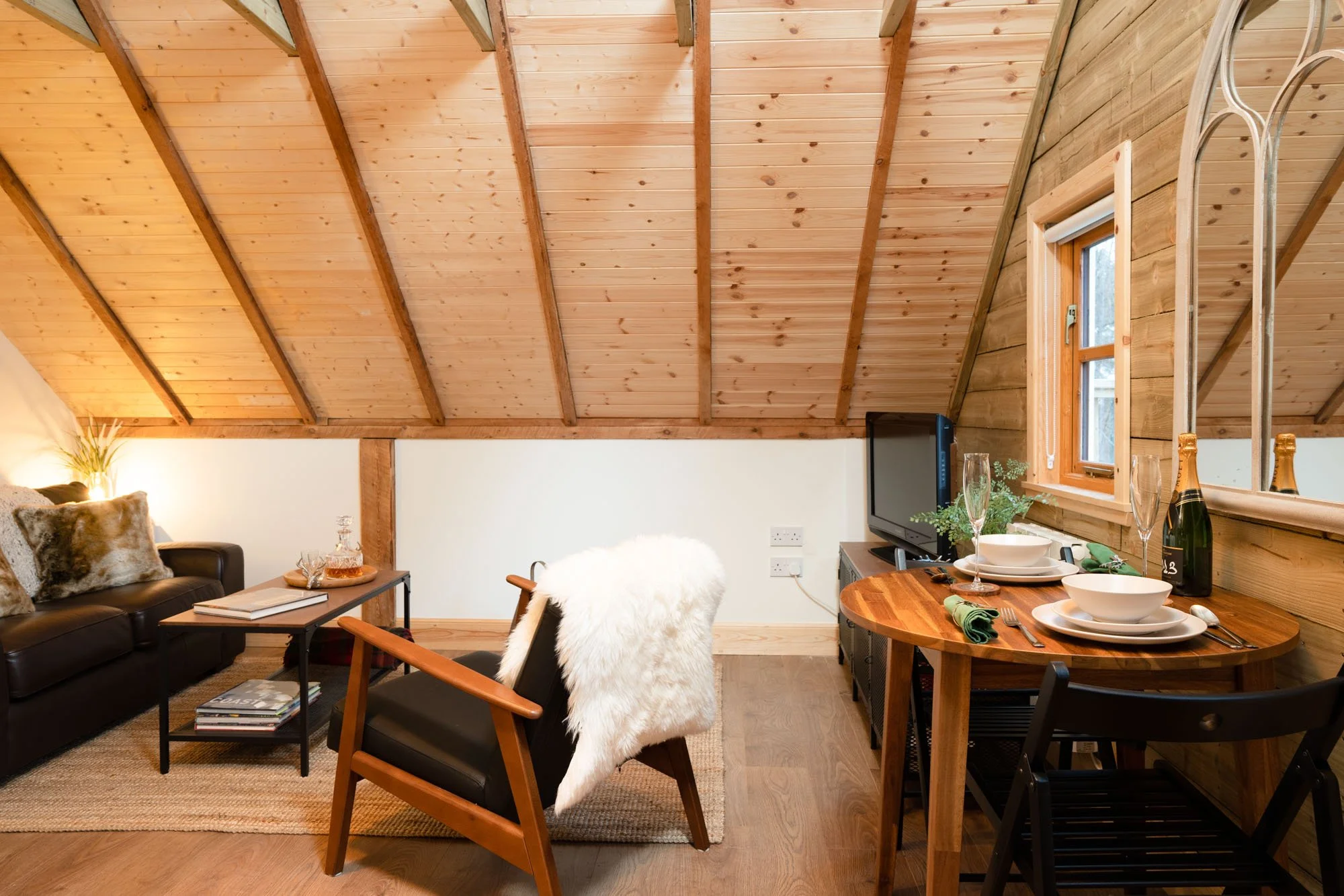 Open-plan living and dining area at The Hayloft, with timber-clad vaulted ceiling, wooden dining table and armchair.