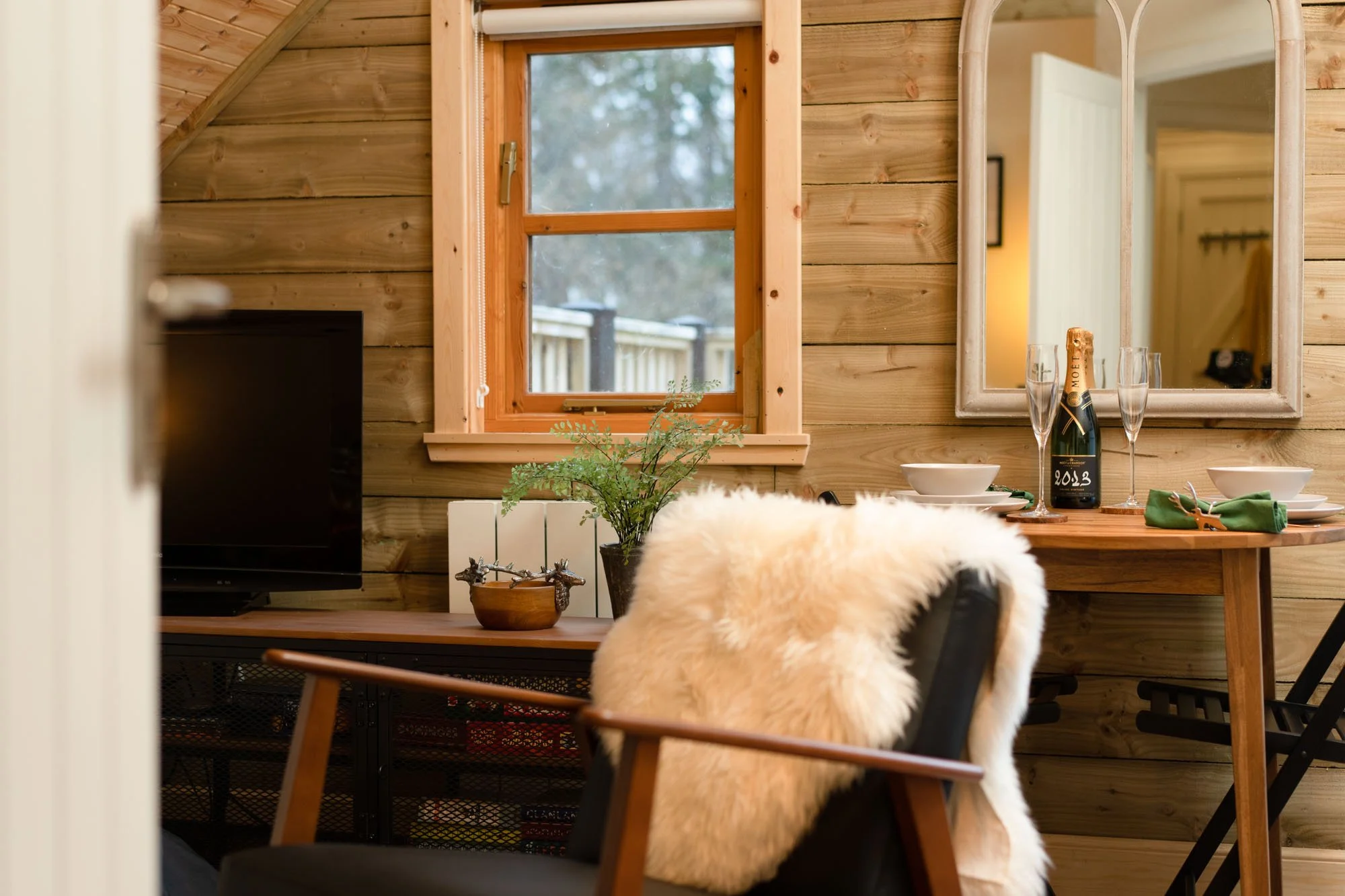 Reading chair beside the kitchen at The Hayloft, with sheepskin throw and views through the wooden-framed window.