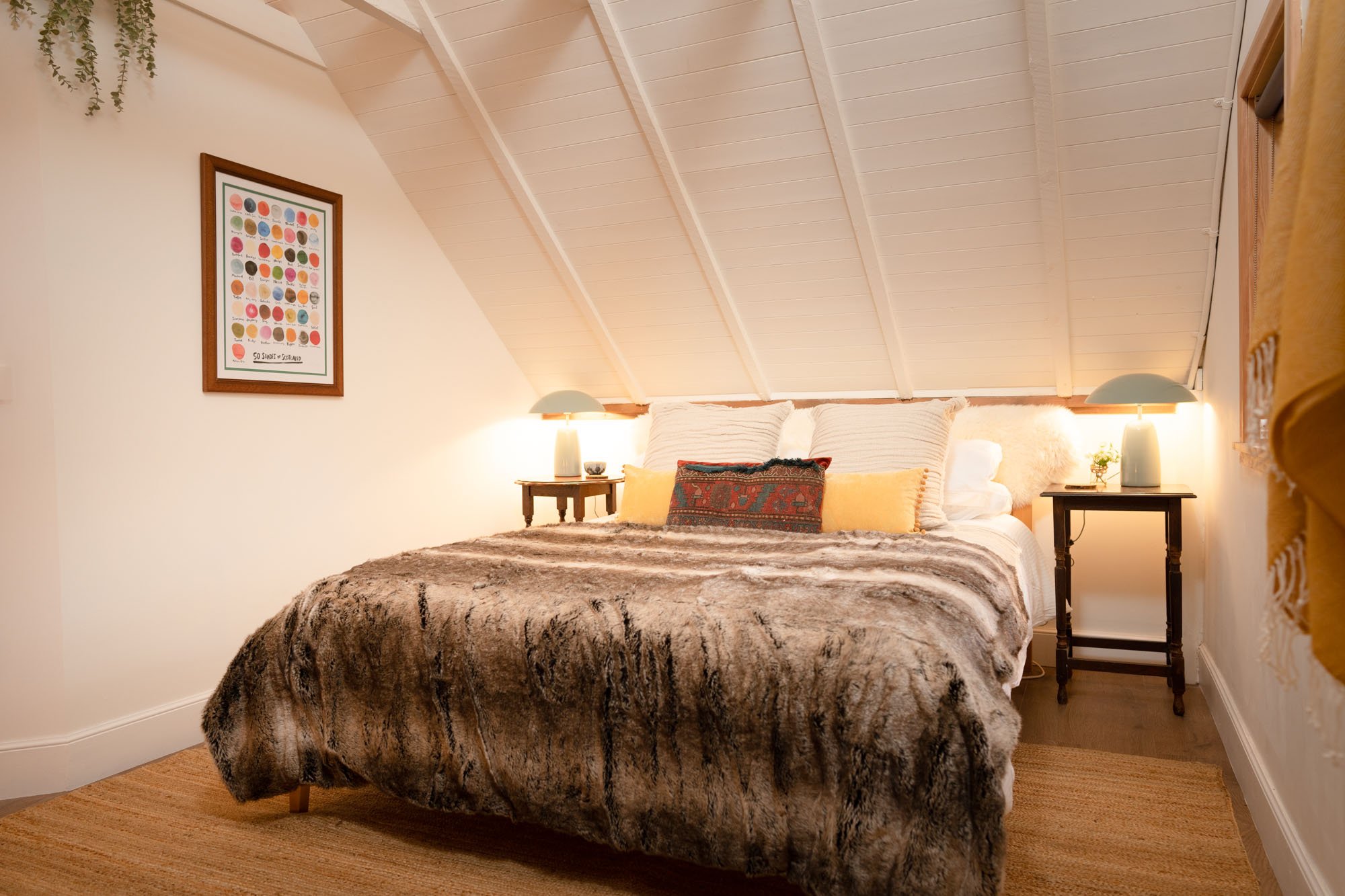Cosy double bedroom at The Hayloft with vaulted white ceiling, warm bedside lighting and soft faux-fur bedspread.