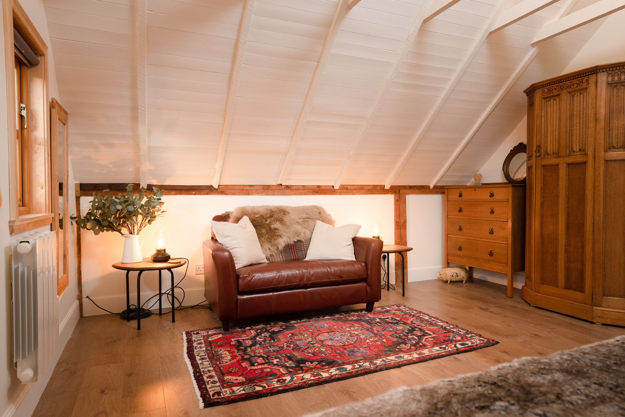 Cosy bedroom seating area at The Hayloft, with leather sofa, patterned rug and low vaulted ceiling.